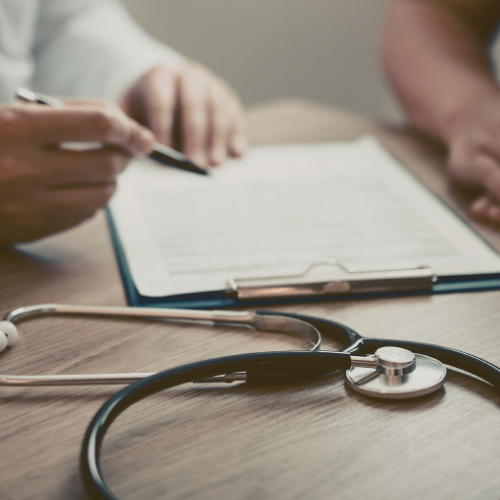 Close-up of a medical consultation with a stethoscope, clipboard, and people discussing documents.
