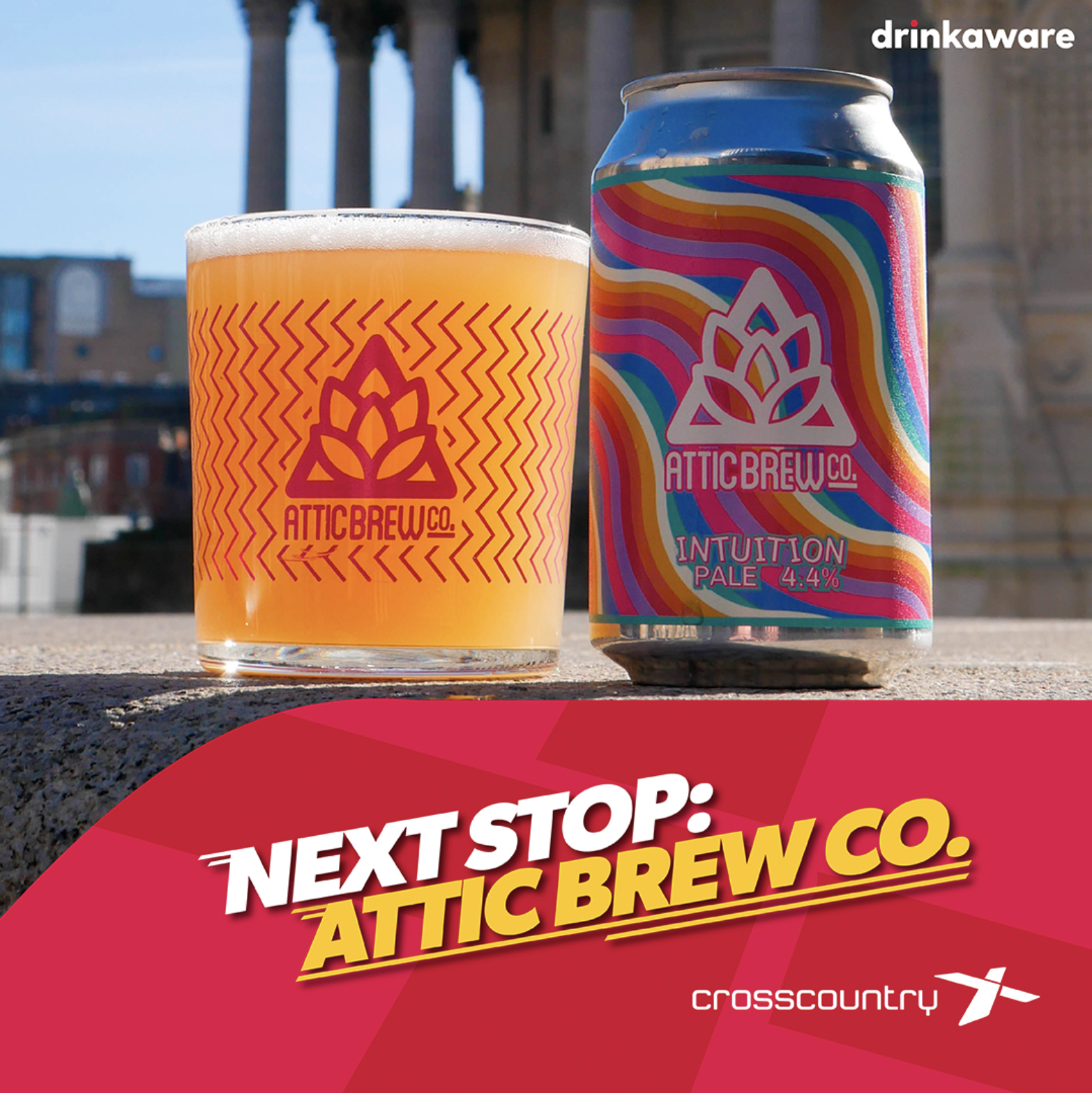 A can and a glass of beer from Attic Brew Co., with the can labeled 'Intuition Pale 4.4%' and featuring colorful, psychedelic swirl patterns, sitting outdoors with a cityscape in the background, and a red banner at the bottom reading 'Next Stop: Atti