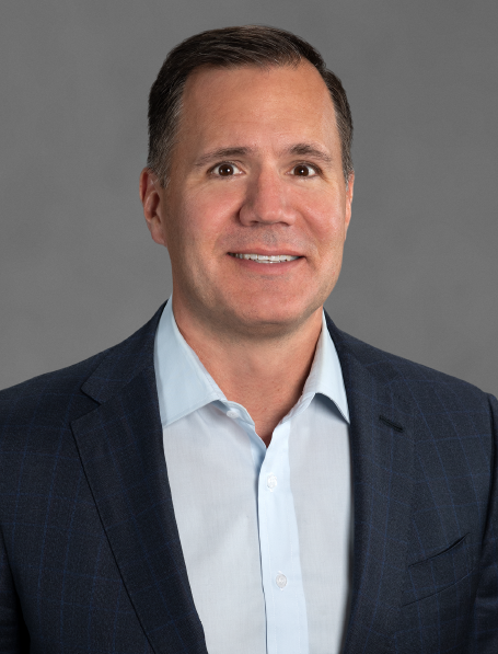 Portrait of a smiling man in a business suit against a gray background.