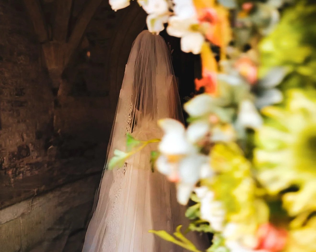 back of bride waiting to enter church to get married photo taken from vantage of peeking behind a floral arrangement