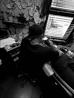 Une personne effectuant un tatouage dans un salon de tatouage, assise devant un miroir avec divers outils et décorations murales.