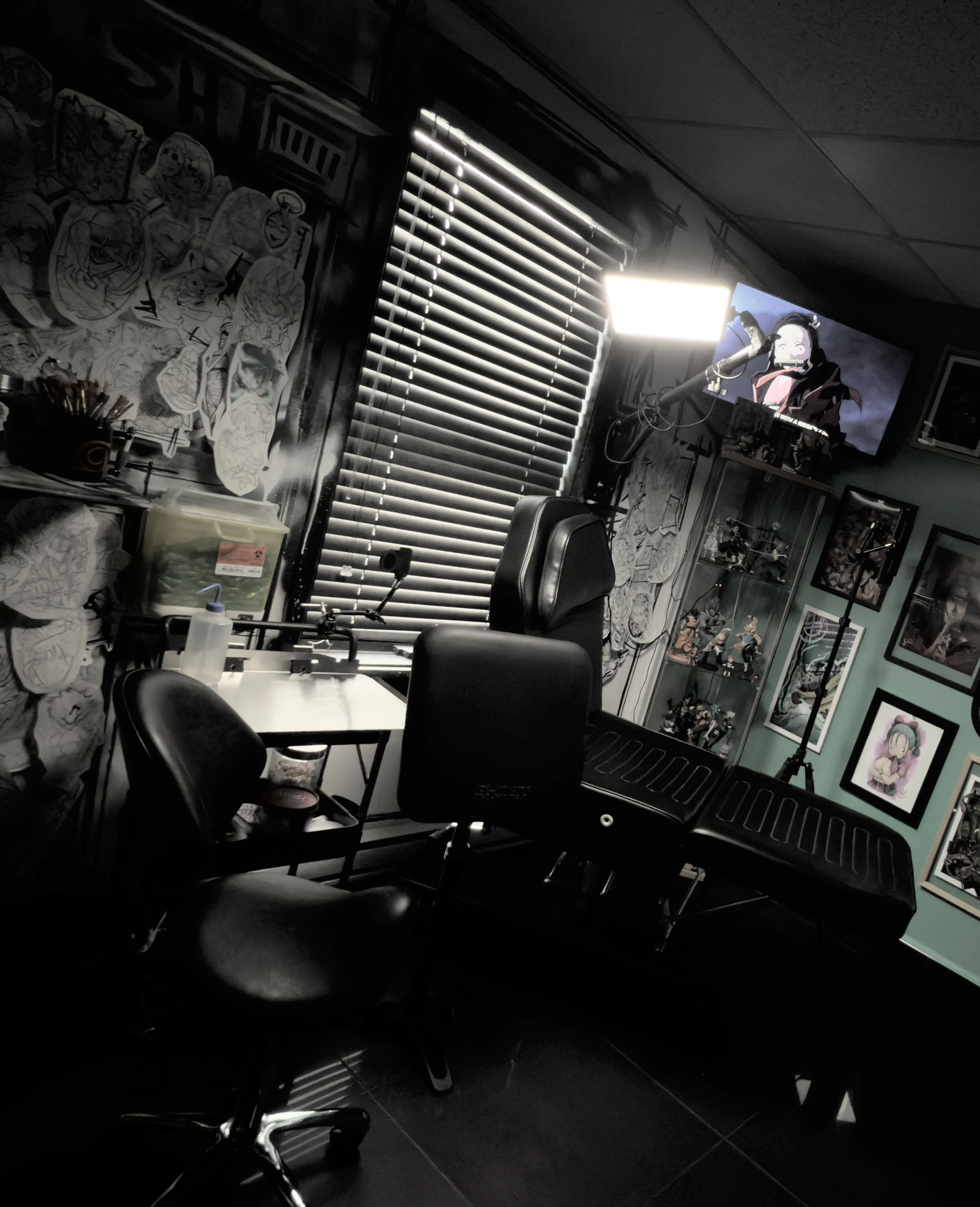 Studio de tatouage avec un fauteuil pour tatouage, une chaise de bureau, étagères avec figurines, murs décorés avec illustrations, une télévision allumée
