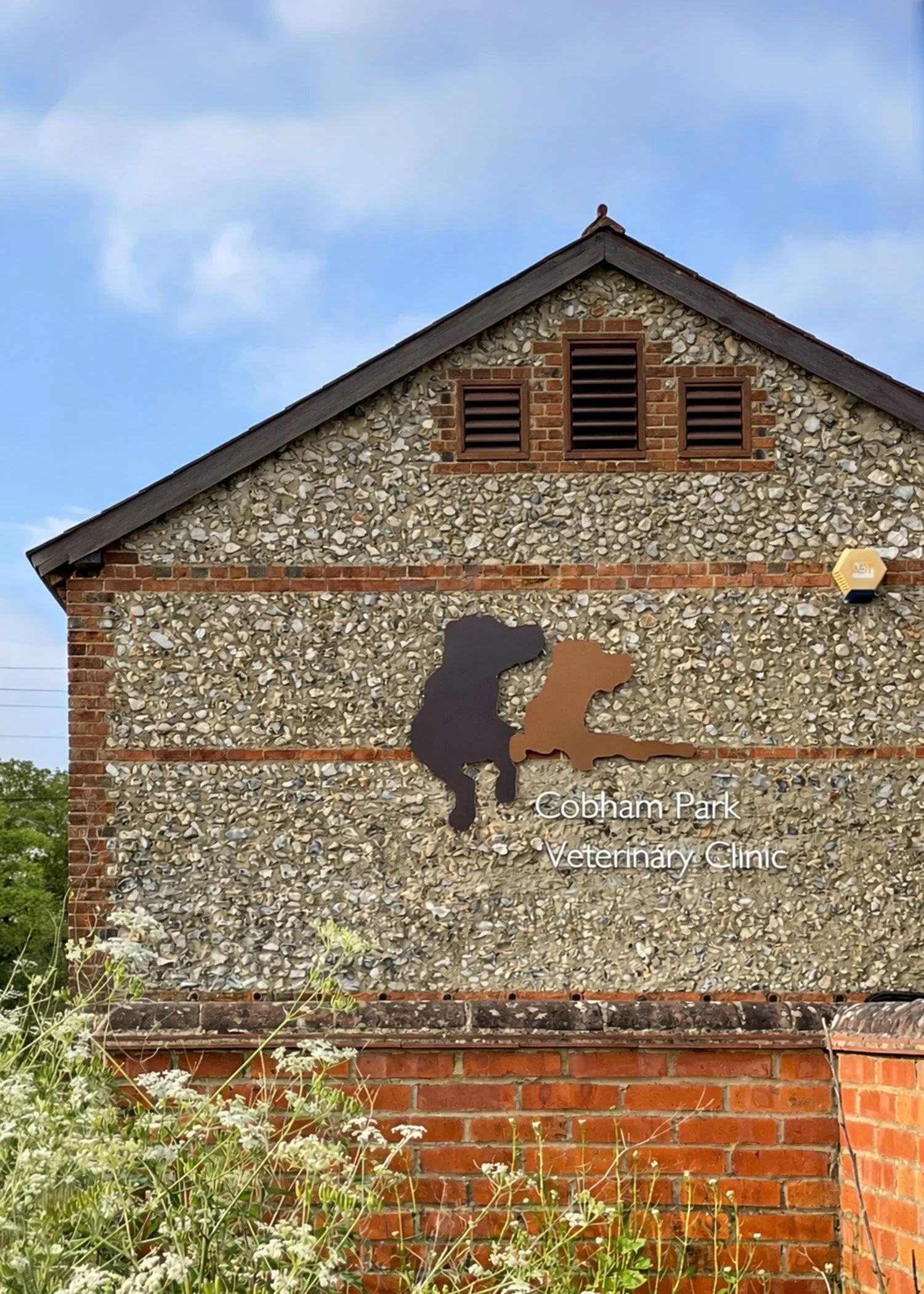 Exterior wall of Cobham Park Veterinary Clinic building with a sign showing a silhouette of a dog and a cat, and the text 'Cobham Park Veterinary Clinic'.