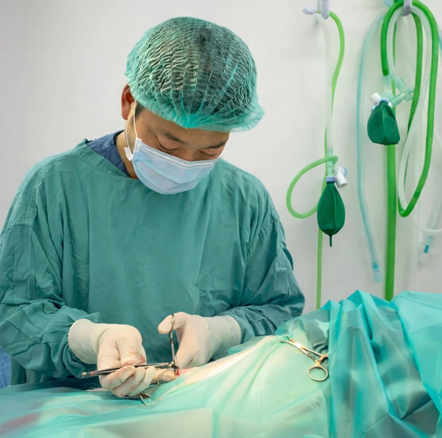 Surgeon in scrubs and mask performing surgery in an operating room.