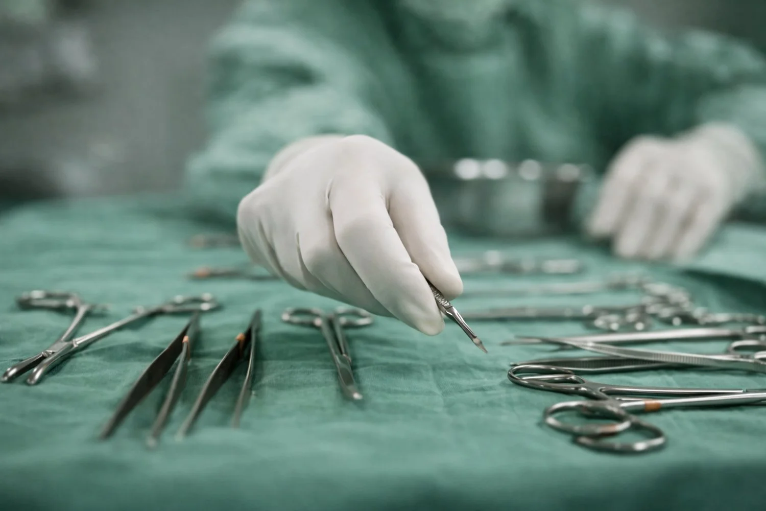 A medical professional wearing white gloves arranging surgical instruments on a green surgical drape.
