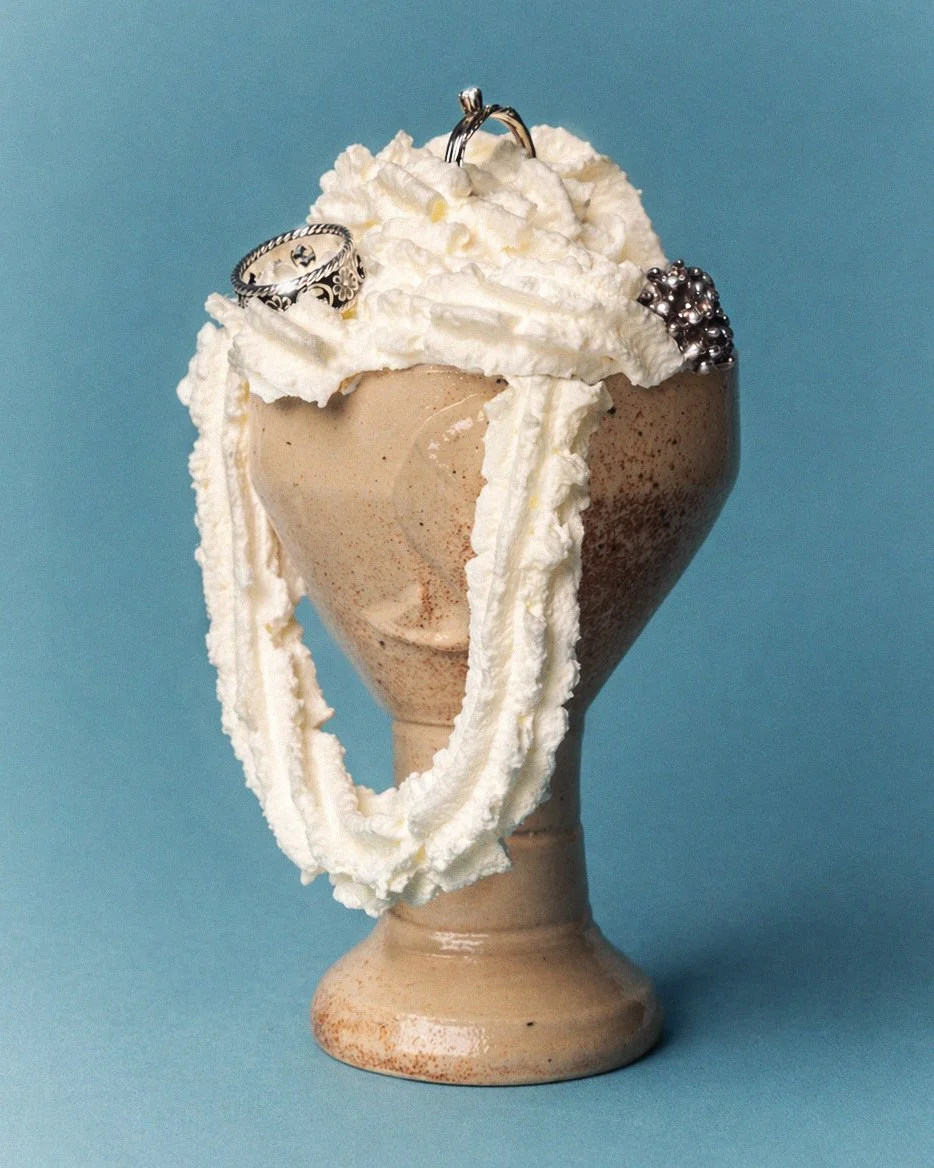Decorative ice cream sundae in a beige goblet with whipped cream, silver beads, and jewelry, against a blue background.