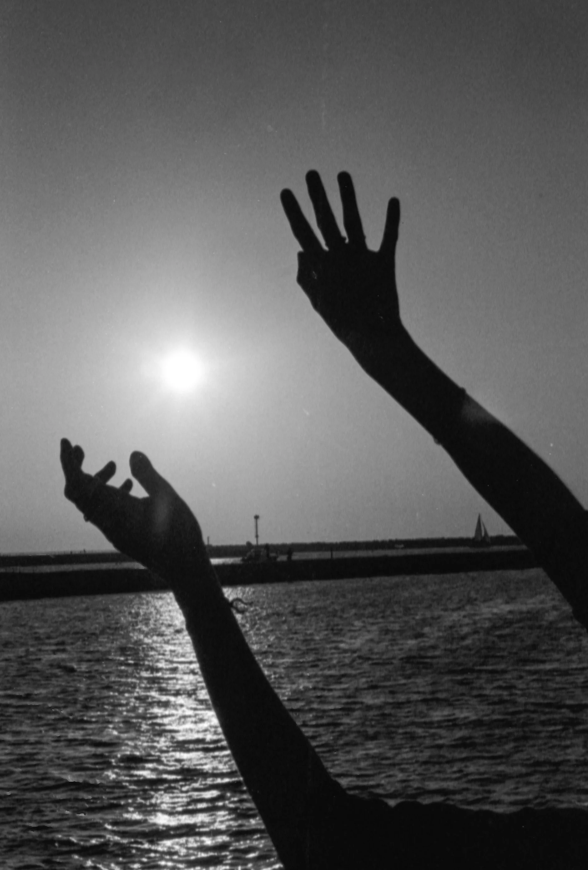 Silhouette of hands raised against the moonlit sky over water, with a lighthouse on the distant shoreline.
