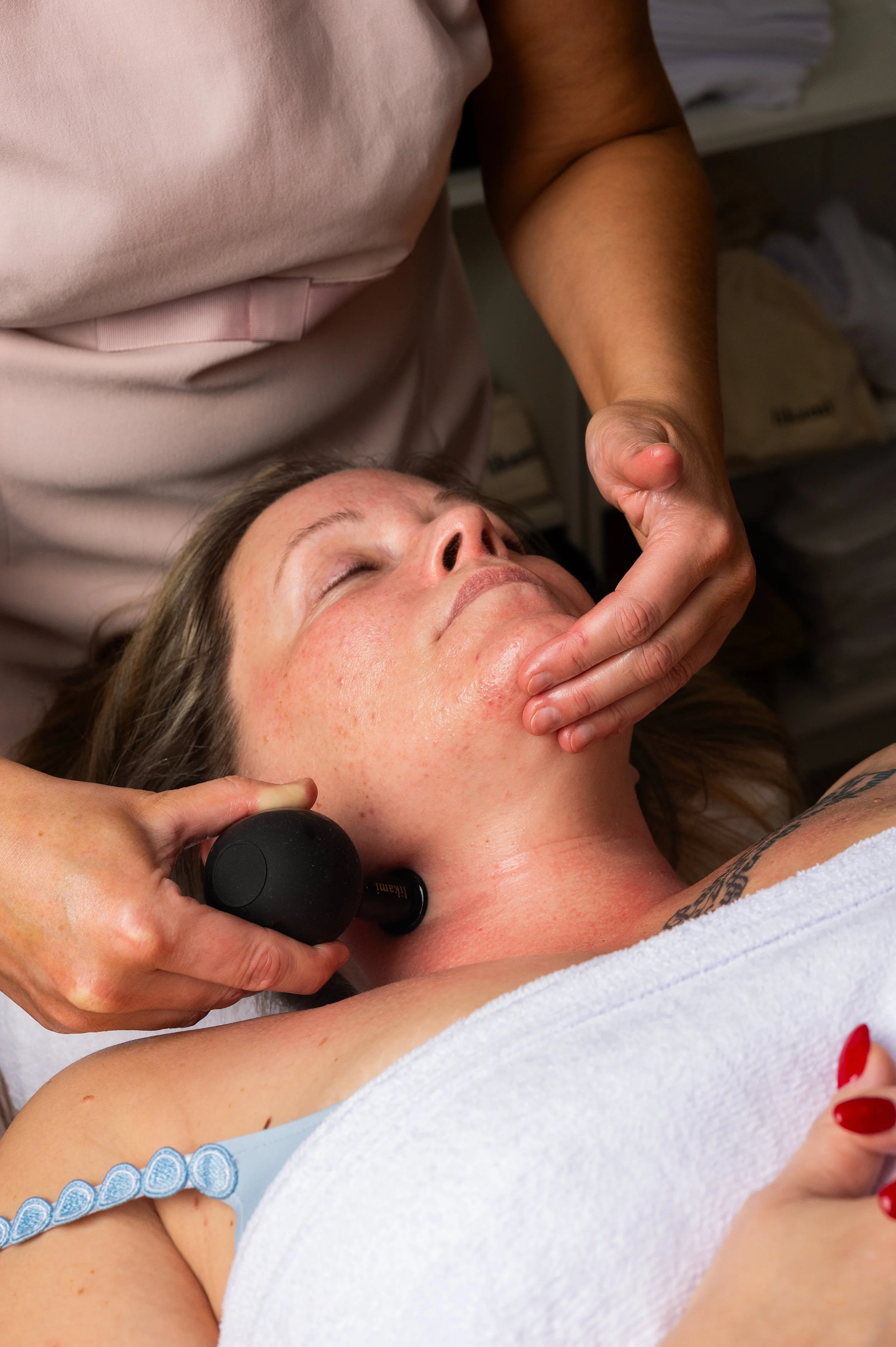 Person receiving facial treatment with a massage device, lying down with closed eyes, in a spa or clinic setting.
