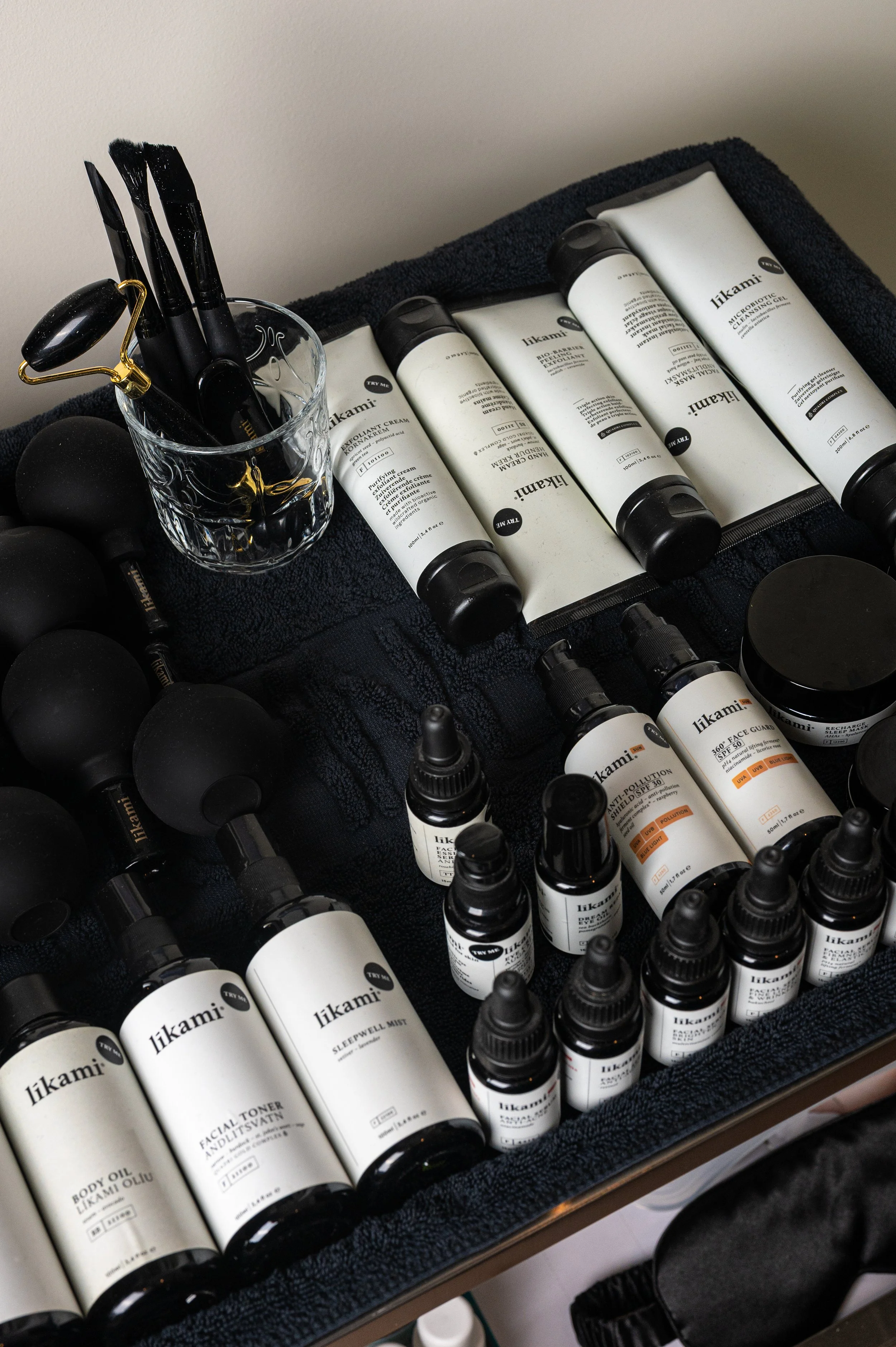 A collection of skincare and beauty products, including various bottles of cream, toner, body oil, face mist, and other skincare items, organized on a black towel surface.