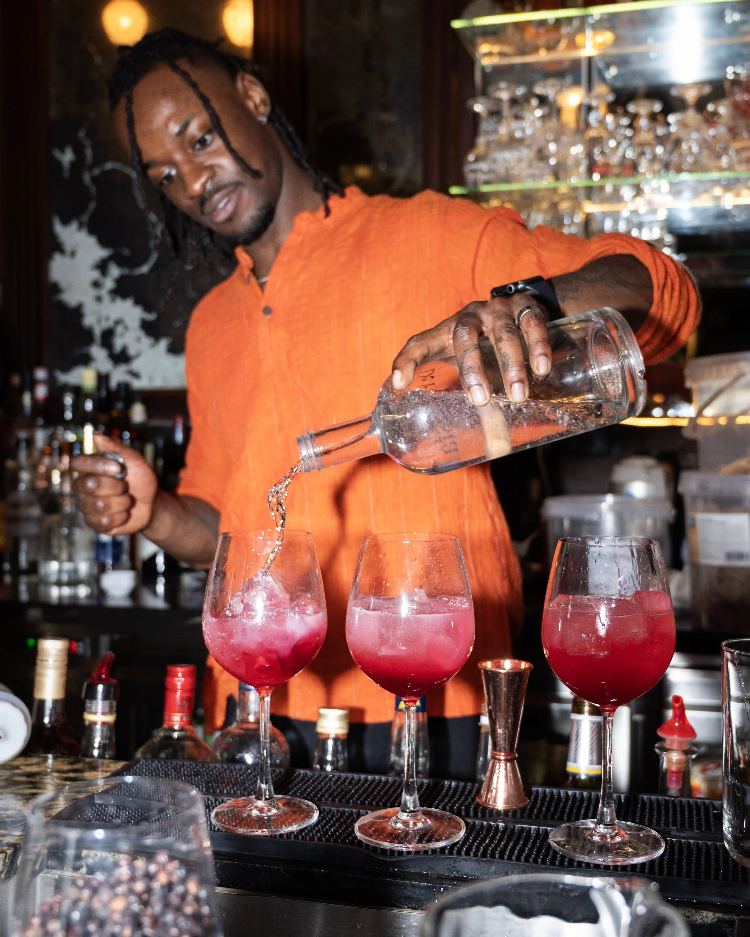 A bartender pouring a red cocktail into glasses at a bar.