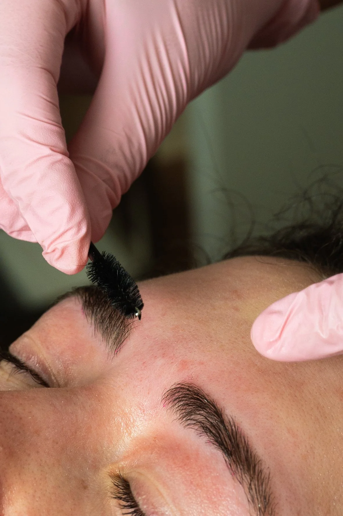 A person receiving a eyelash extension treatment with a technician applying false eyelashes to the person's upper eyelid while wearing pink gloves.