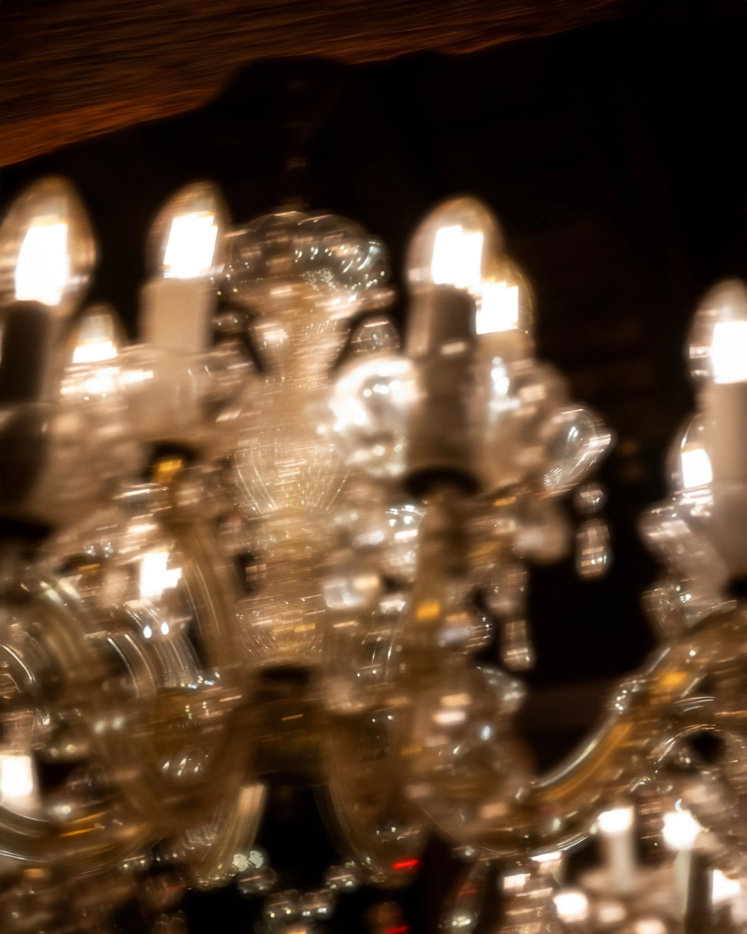 Close-up of a chandelier with crystals and glowing lights, covered by a dark shade.