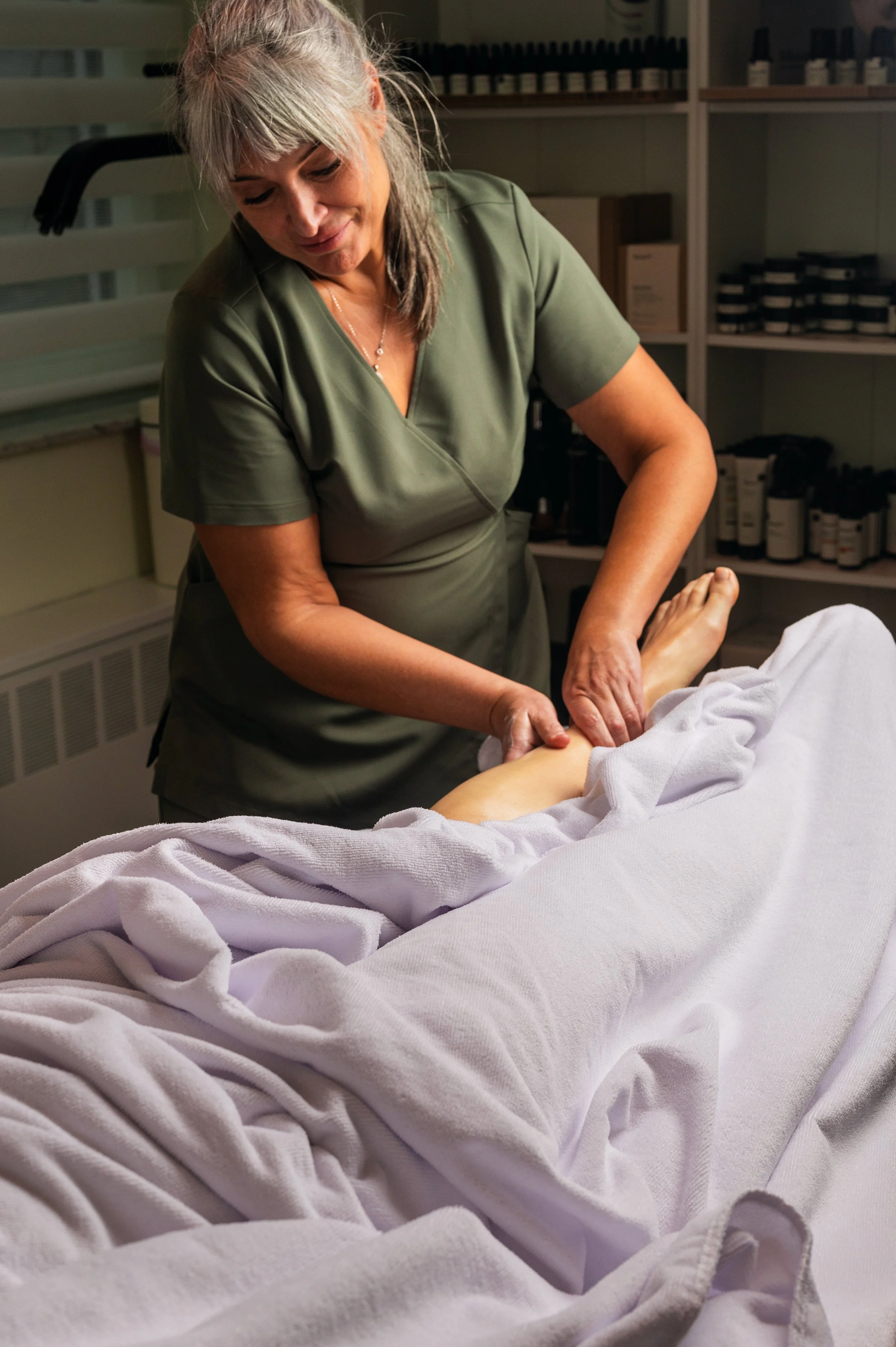 A massage therapist performing a leg massage on a person lying on a massage table, with towels covering the person's body.