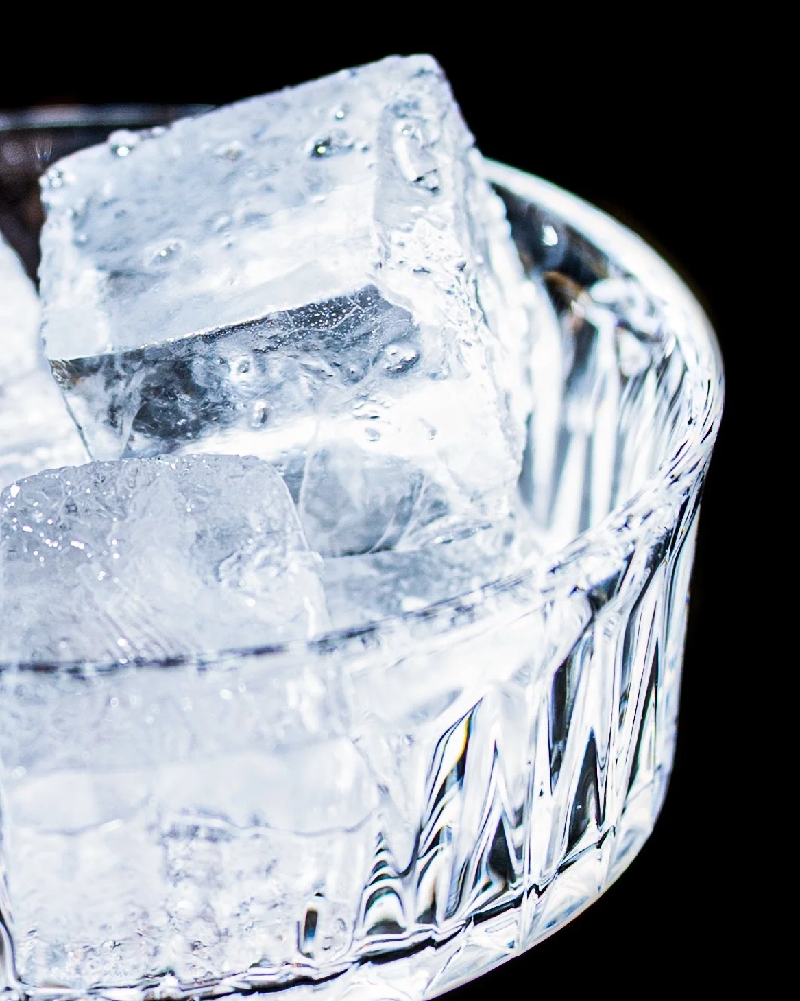 Close-up of clear ice cubes in a decorative glass bowl against a black background.