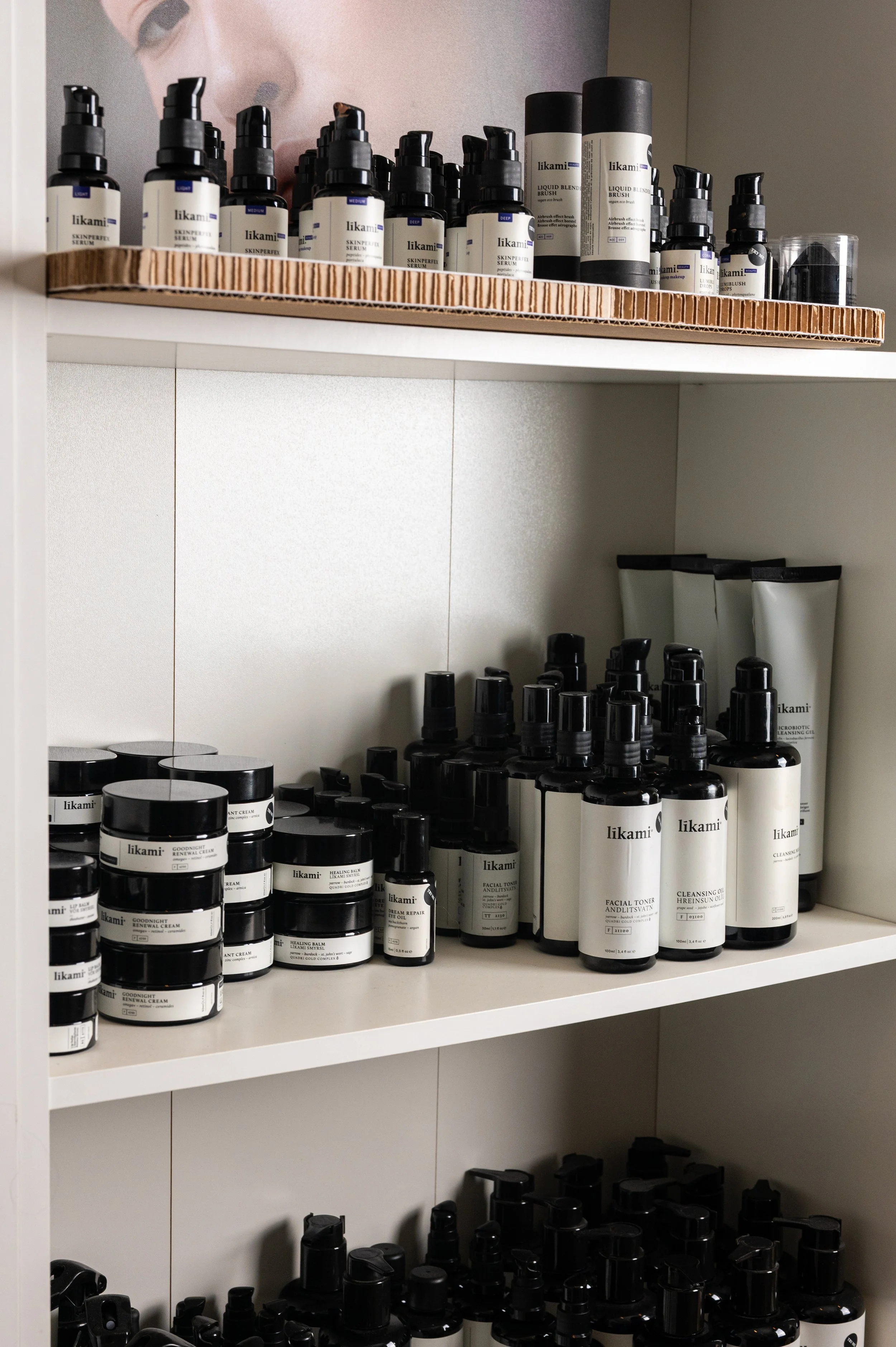 Shelves filled with various skincare and cosmetic bottles and jars, including cleansers, toners, and creams, on a white shelving unit against a wall.
