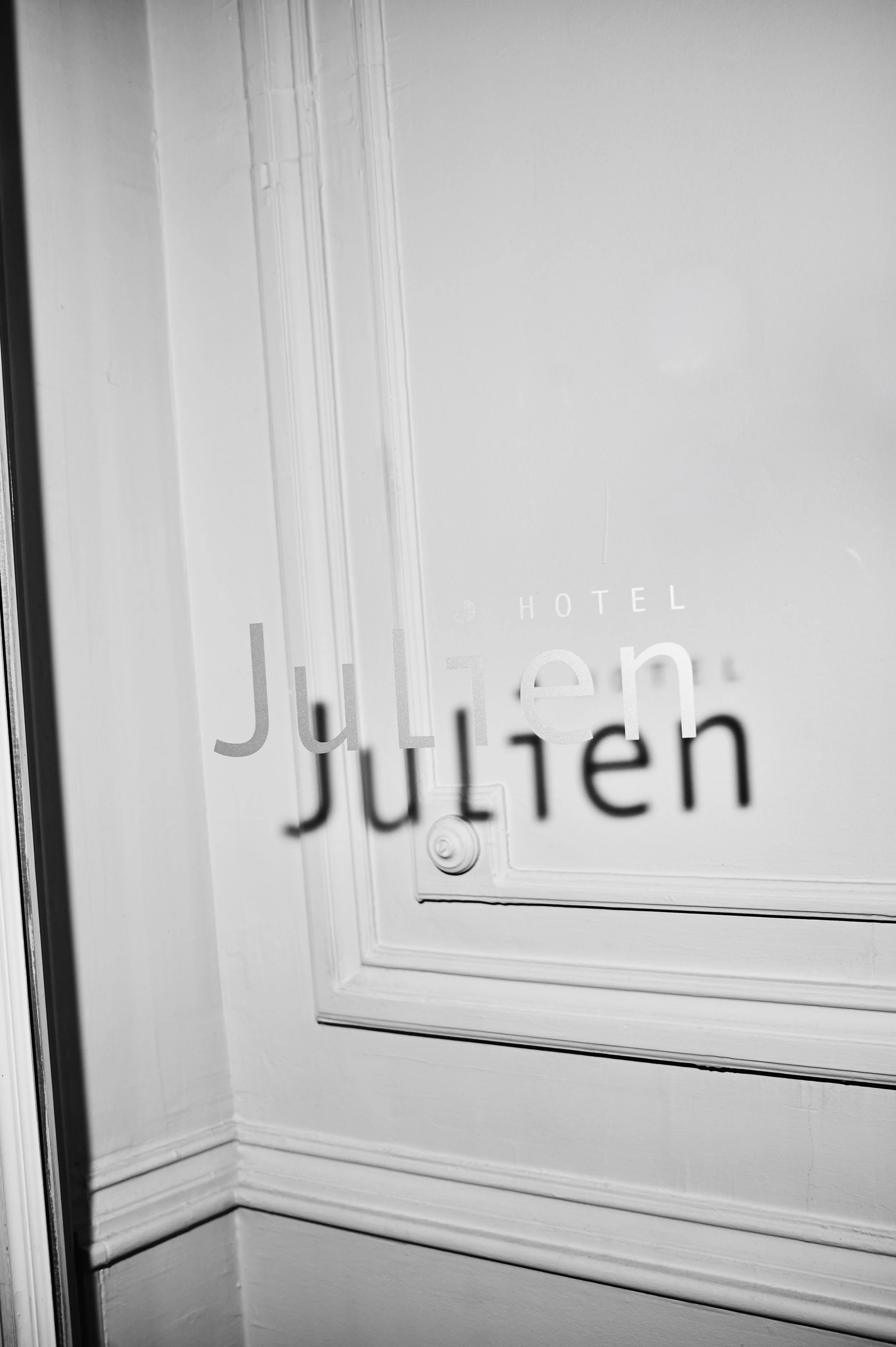 Close-up view of a white door with glass panel. The door has the word 'Julien' written on it, indicating it is likely a hotel room door.