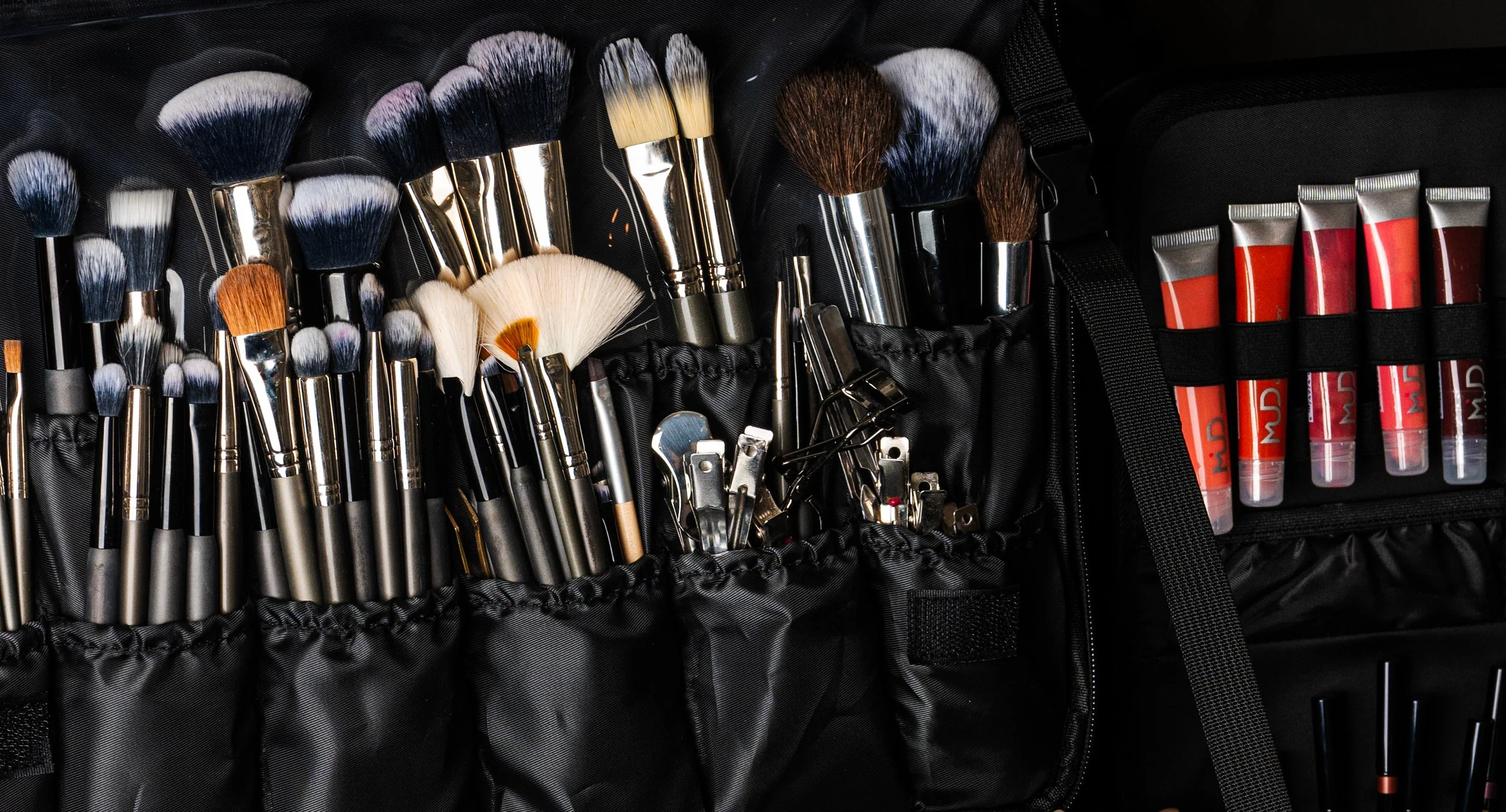 A collection of makeup brushes and tubes of lipstick in a black carrying case.
