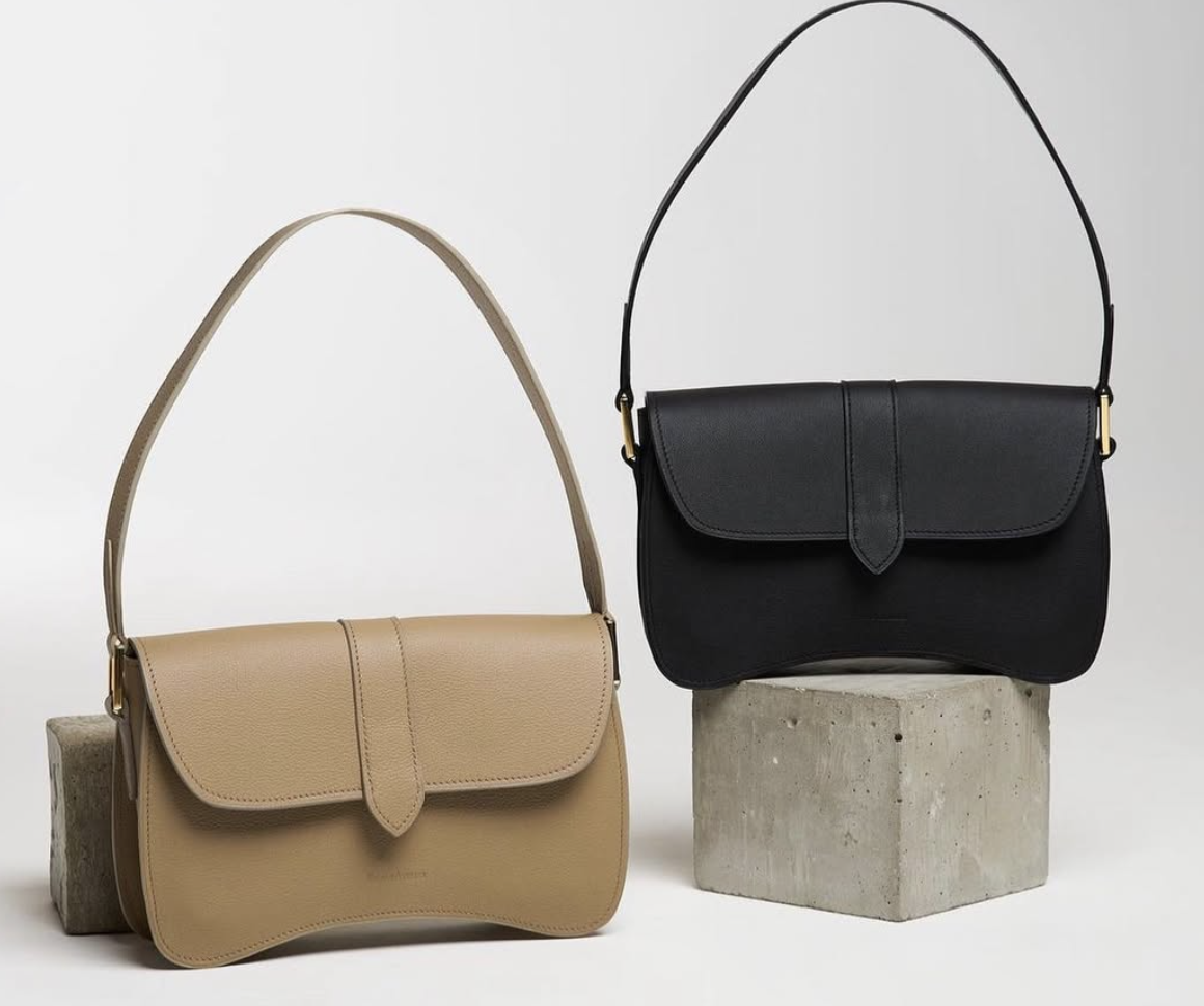 Deux sacs à main en cuir, un beige et un noir, posés sur des blocs de béton avec un fond gris clair.