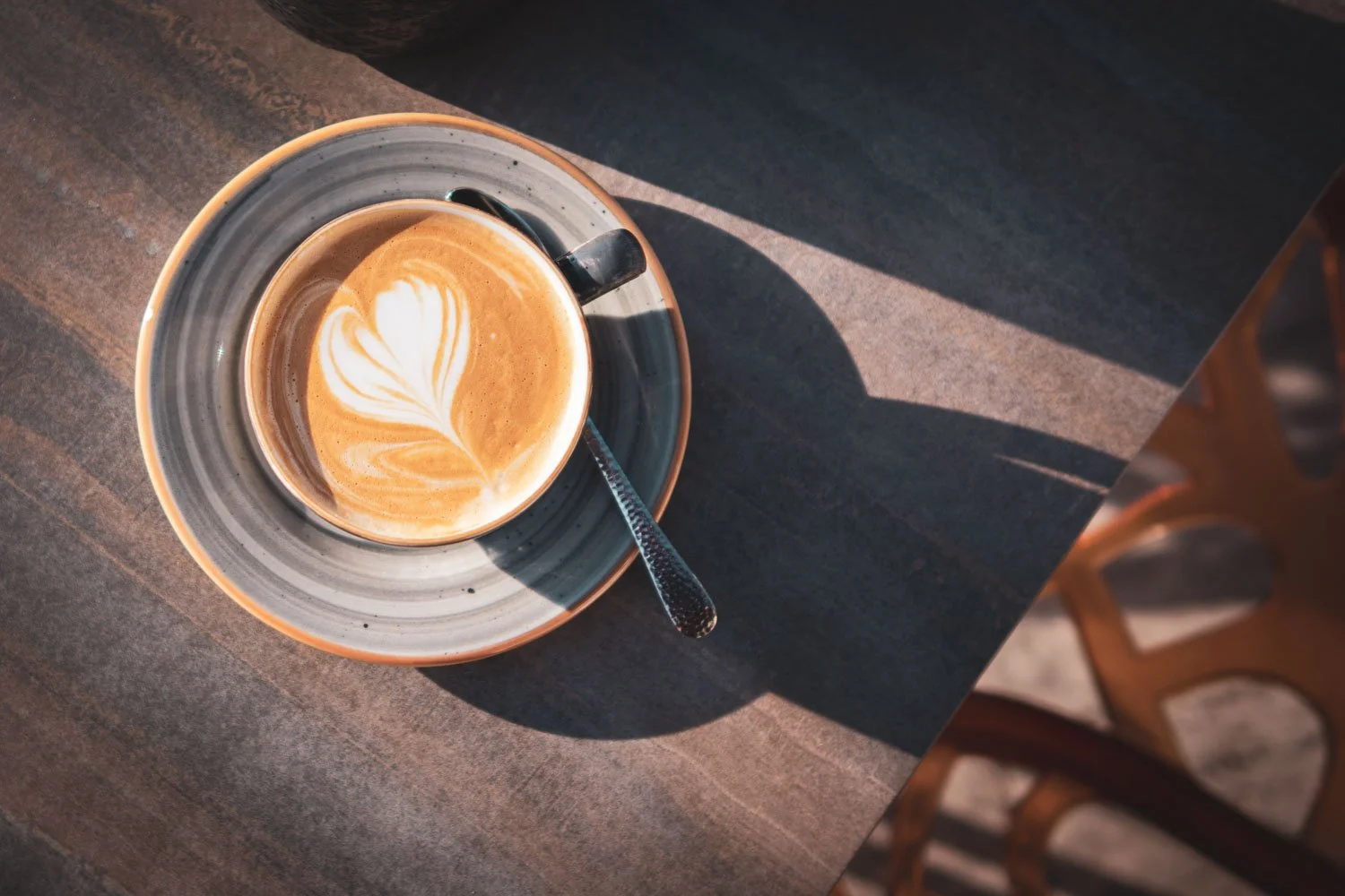 Tasse Kaffee mit Herz-Muster auf cremigem Milchschaum, auf einem dunkelbraunen Holztisch, mit Sonnenlicht und Schatten