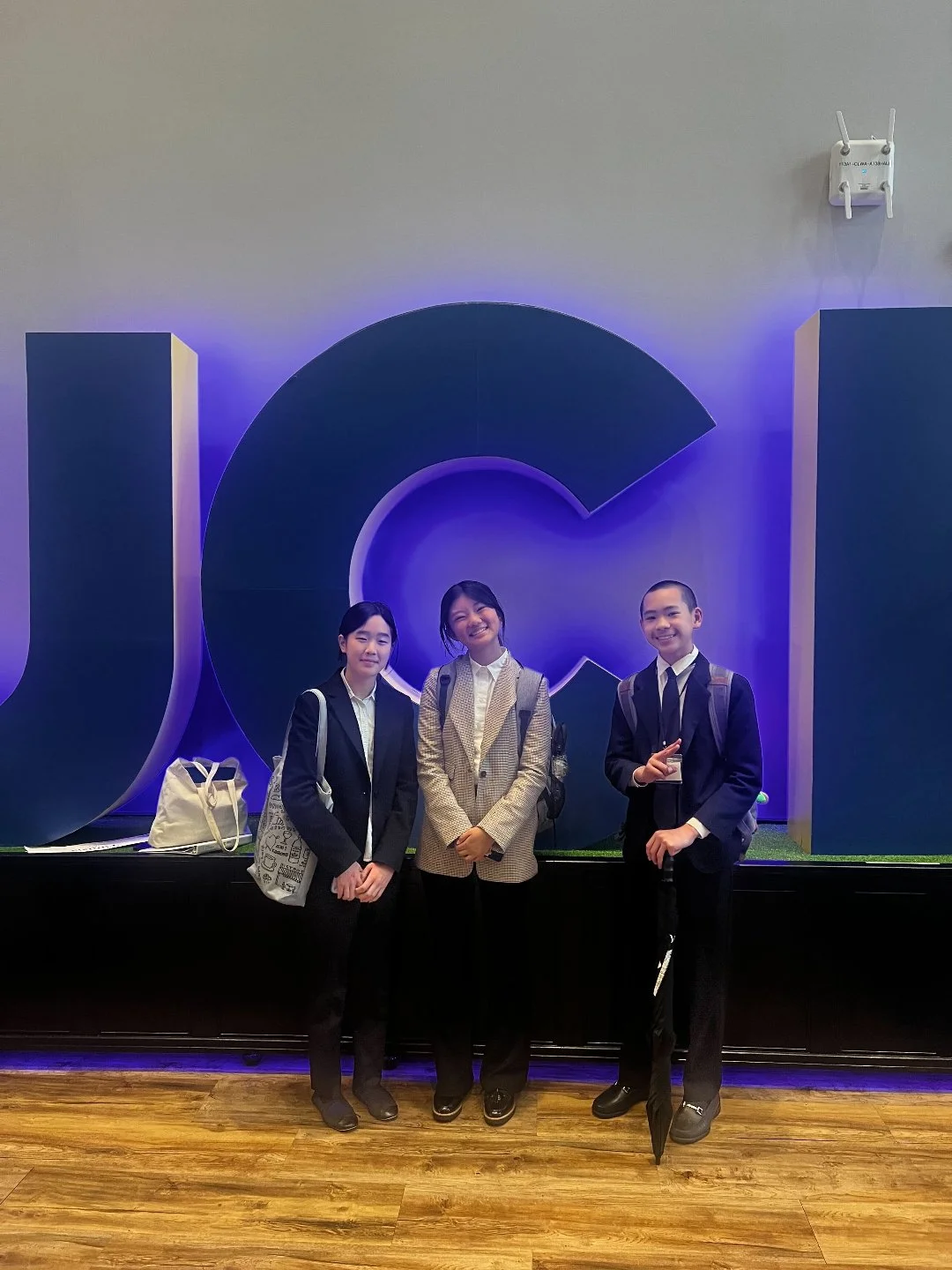 Three students in business attire standing in front of a large, illuminated Google logo.