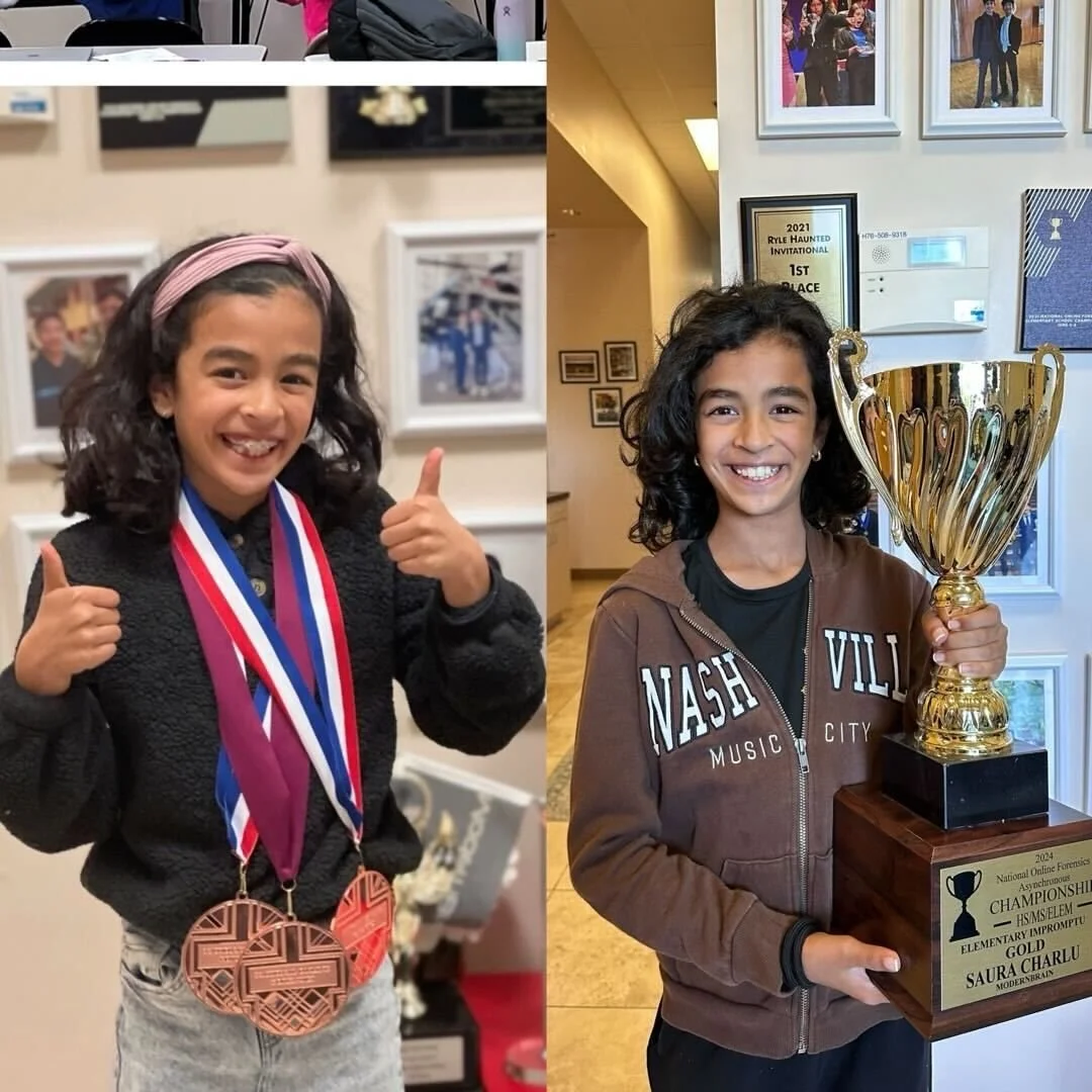 Two young girls smiling, each with awards. The girl on the left has medals around her neck and thumbs up. The girl on the right is holding a large gold trophy and is smiling.