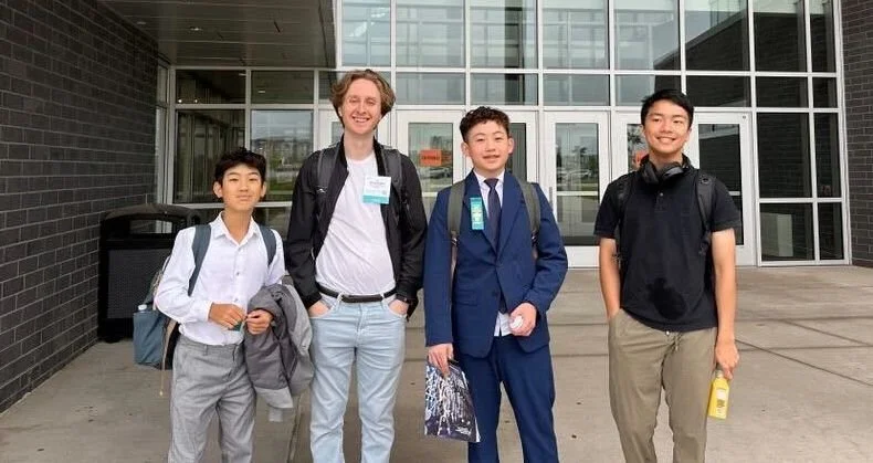 Four boys and one adult standing outside a modern building, posing for a photo.
