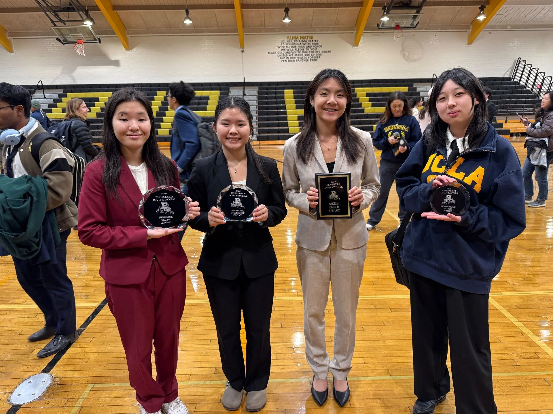 Four young women standing on an indoor basketball court, each holding an award plaque, smiling at the camera after an event.