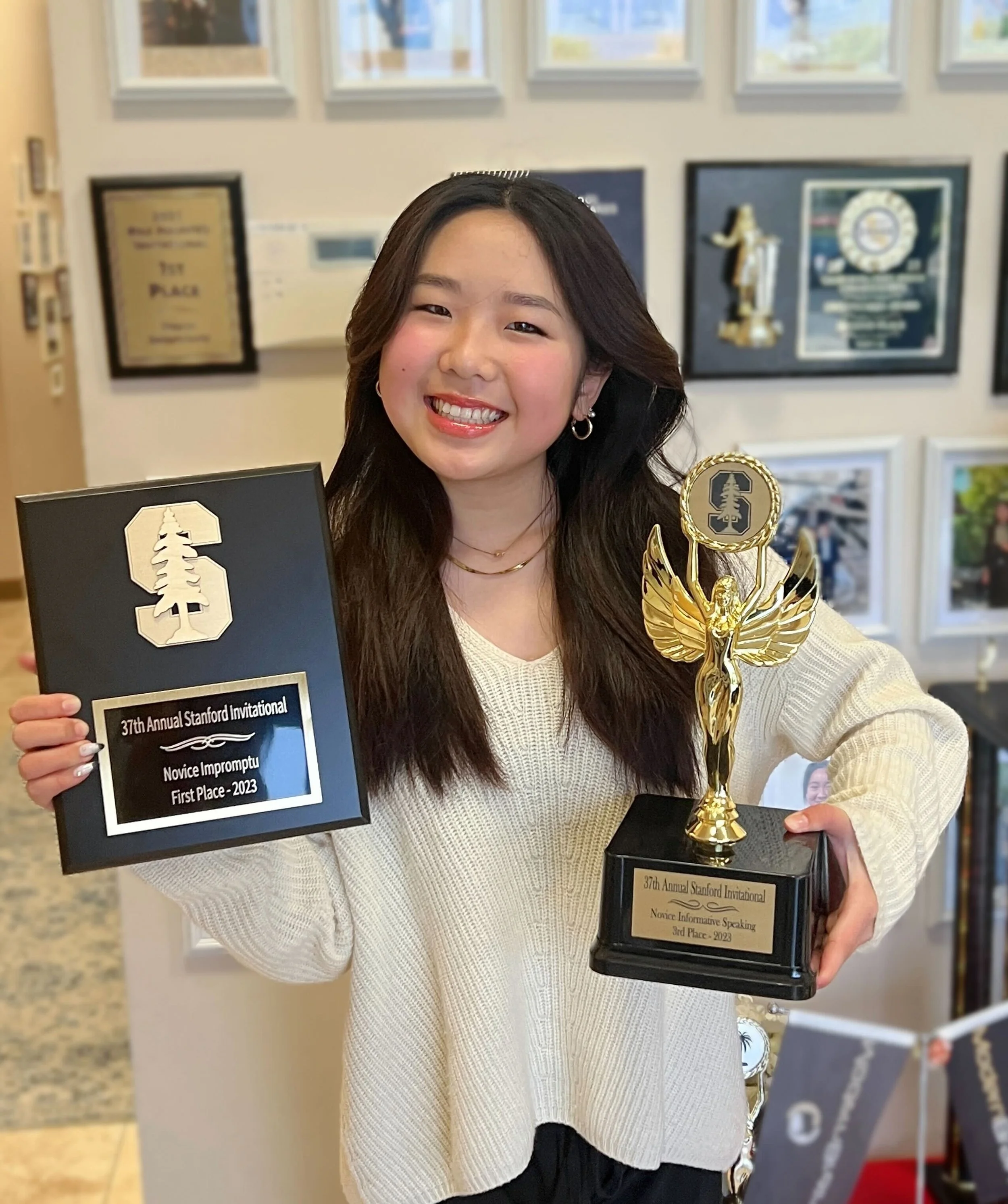 Young woman smiling and holding a plaque and a trophy at an awards ceremony.