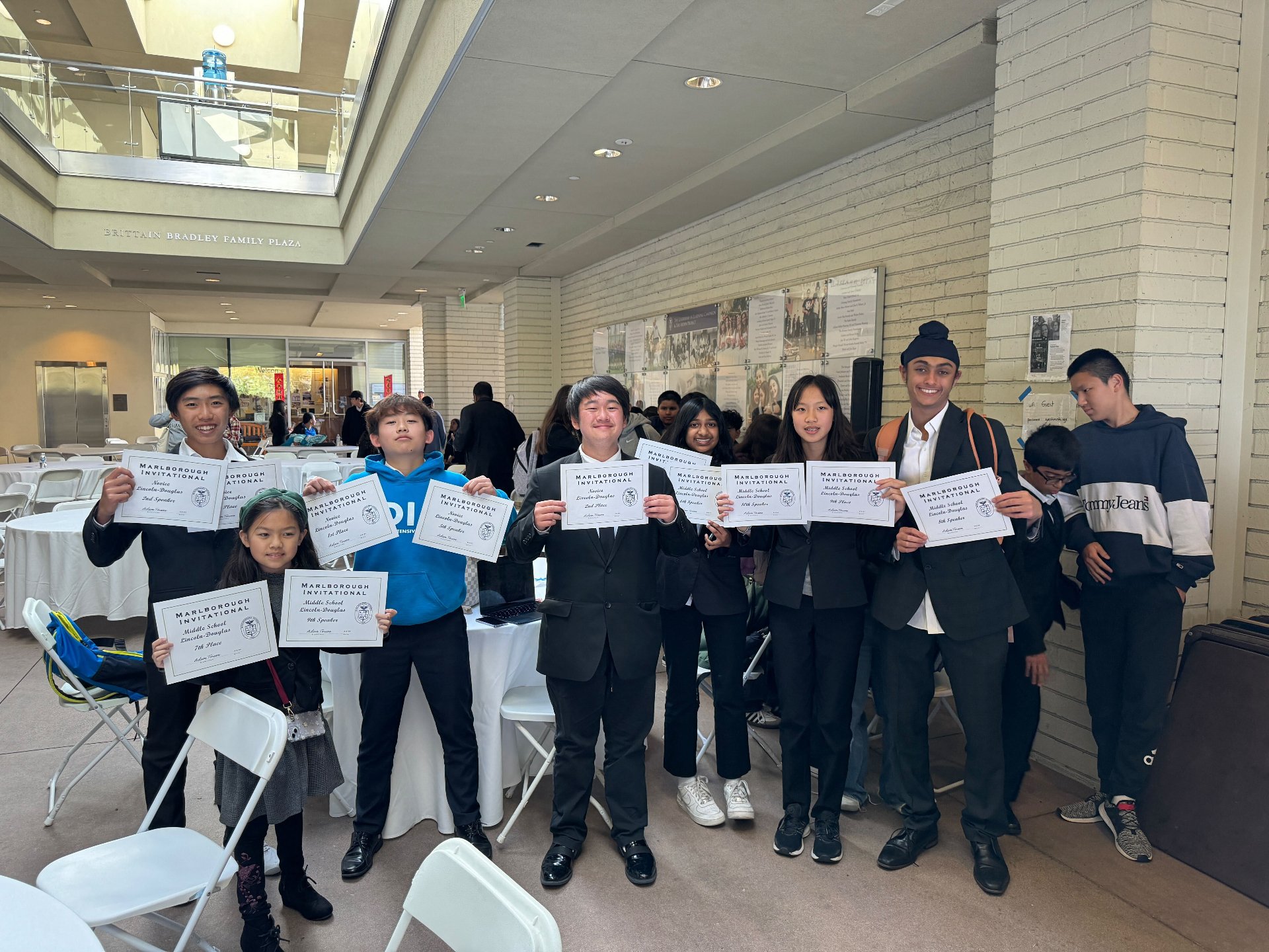 Group of children and teenagers holding certificates at an indoor event, smiling for a photo.