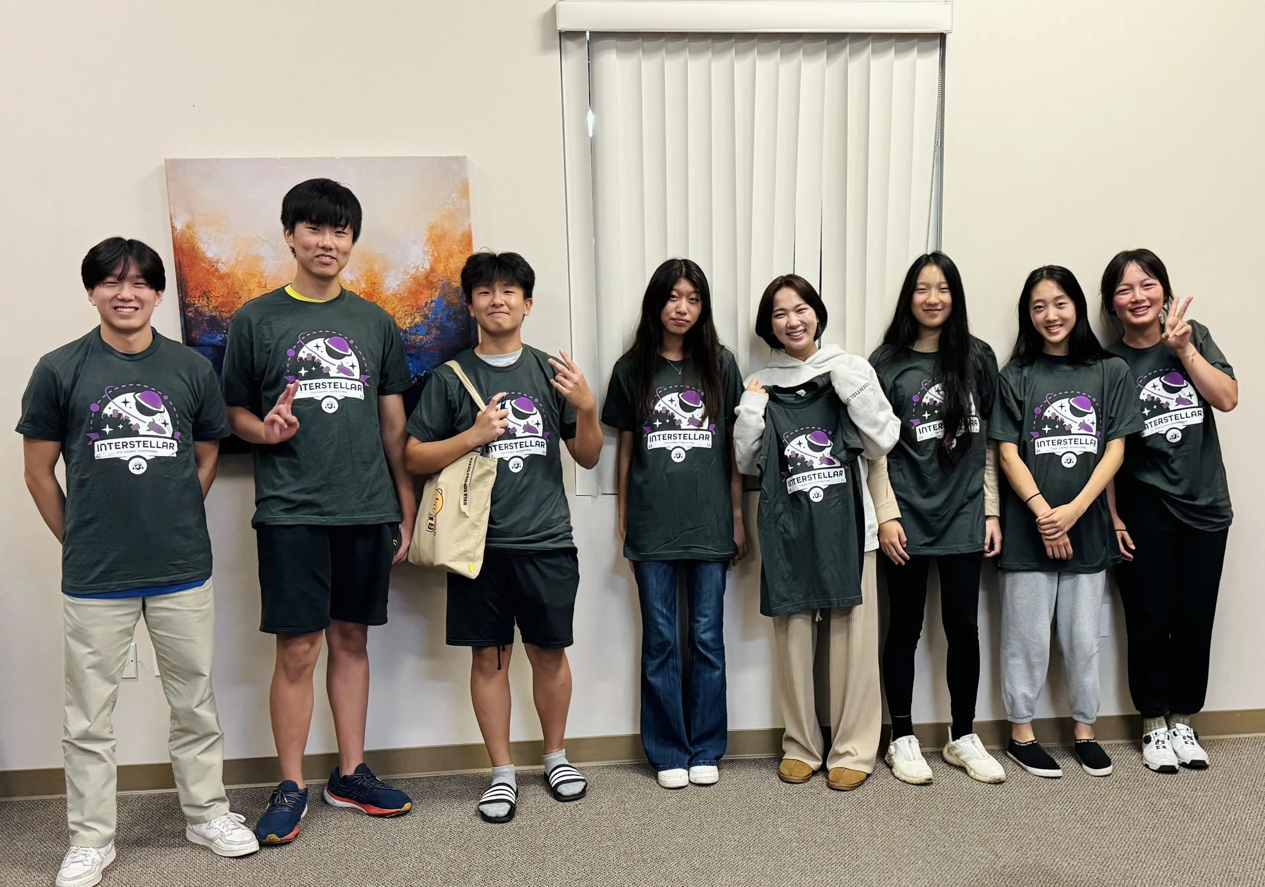 Group of nine young people standing indoors, wearing matching green T-shirts with an 'Interstellar' logo, posing for a photo.