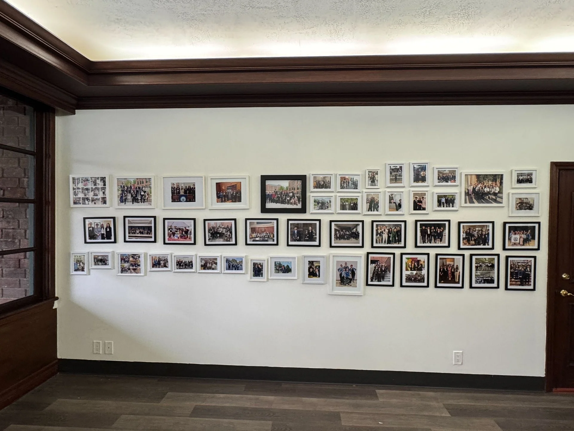 Wall decorated with numerous framed photographs arranged in rows inside a room with wood trim.