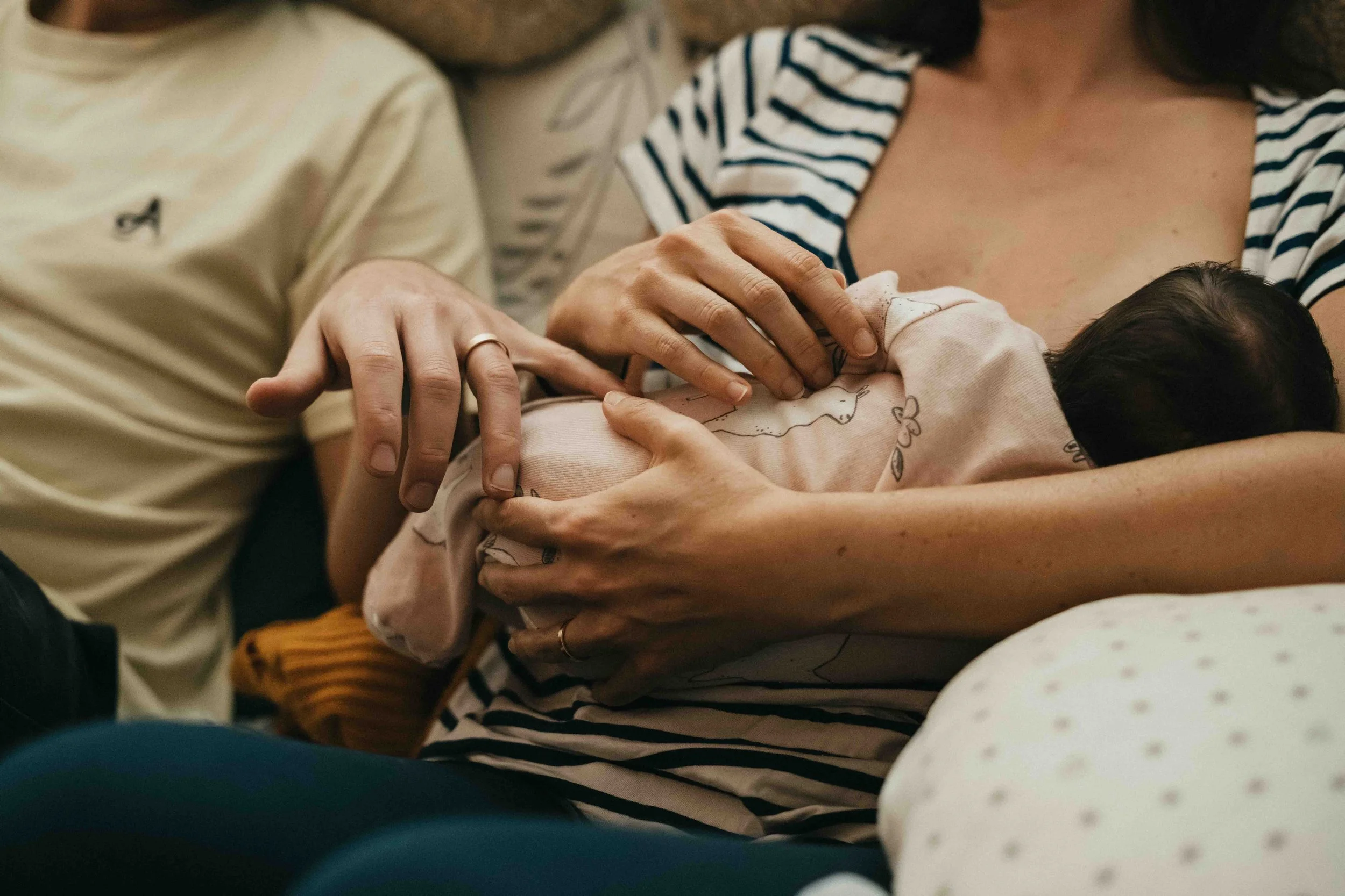 Eine Frau hält ein Baby im Arm, während ein Mann und eine Frau neben ihr sitzen, vermutlich bei einer Geburt im Krankenhaus.