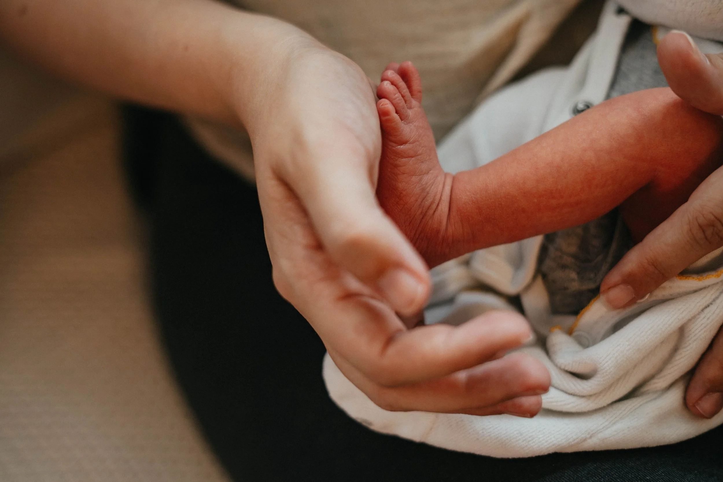 Liebevolle Detailaufnahme von winzigen Babyfüssen in den Händen der frischgebackenen Eltern während eines Wochenbett-Shooting