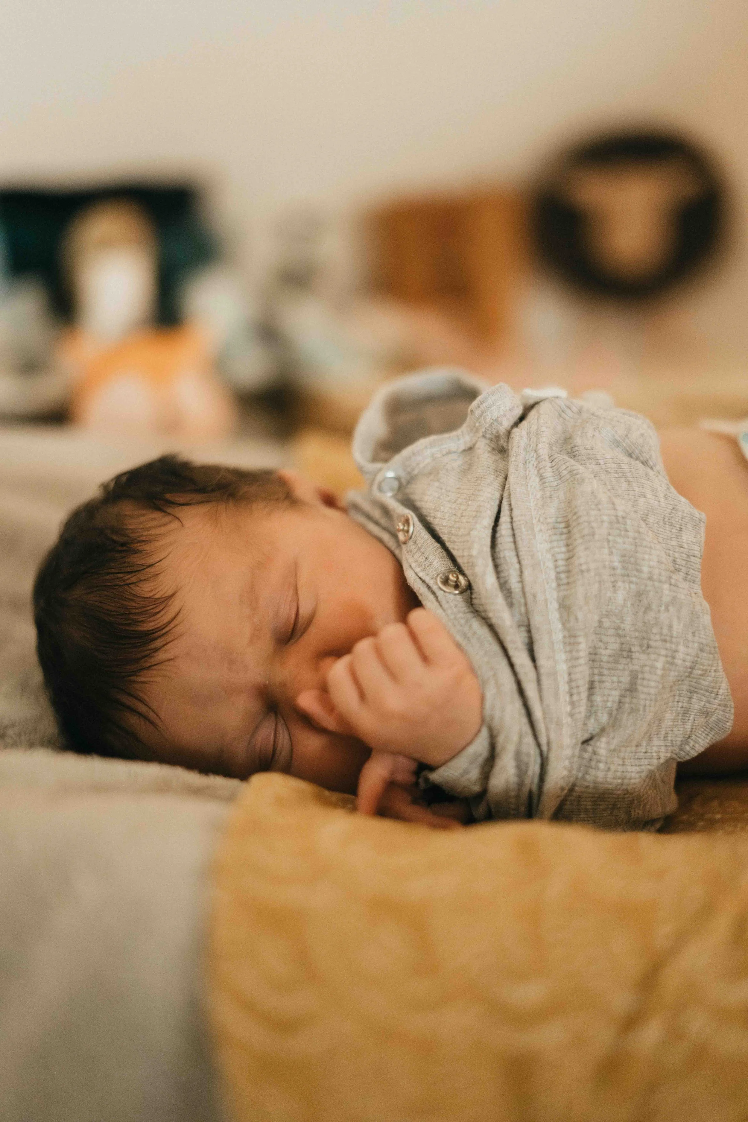 Ein schlafendes Baby liegt auf einem Bett, trägt einen grauen Pullover und hat dunkle, nasse Haare.