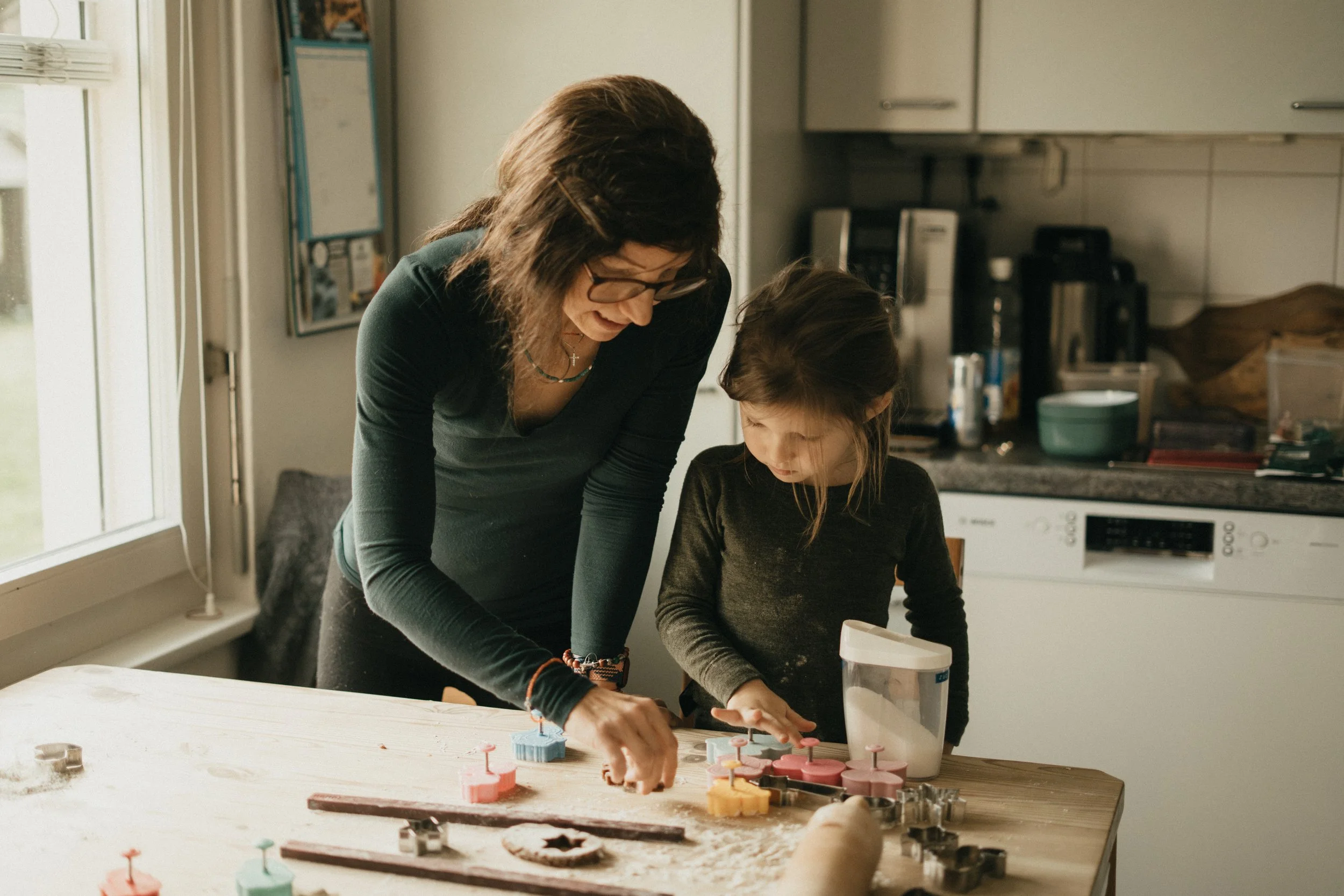 Eine Frau und ein Mädchen spielen zusammen mit Keksausstechern auf einem Tisch in der Küche.