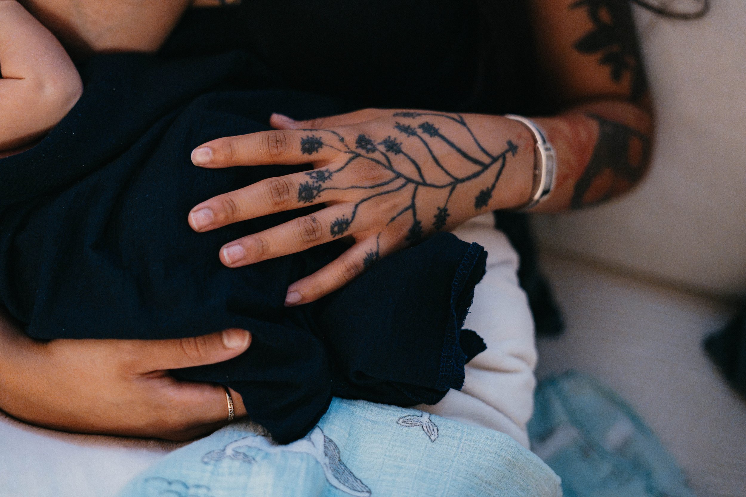 Detailaufnahmen einer tätowierten Hand, die ein Baby auf einer hellblauen Decke hält