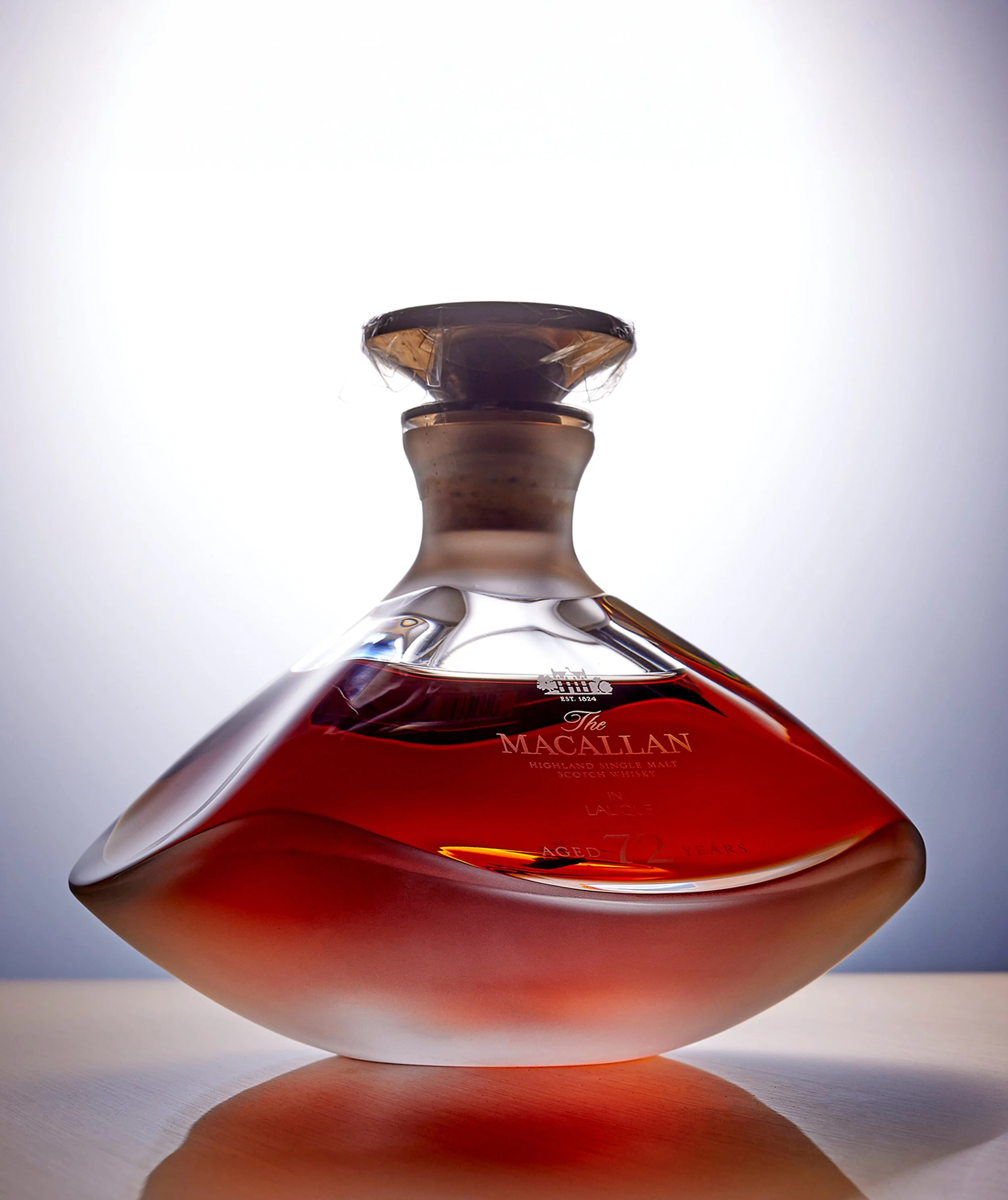 Close-up of a bottle of Macallan Highland Single Malt Scotch Whisky, placed on a flat surface with a plain light background, photographed from a low angle.