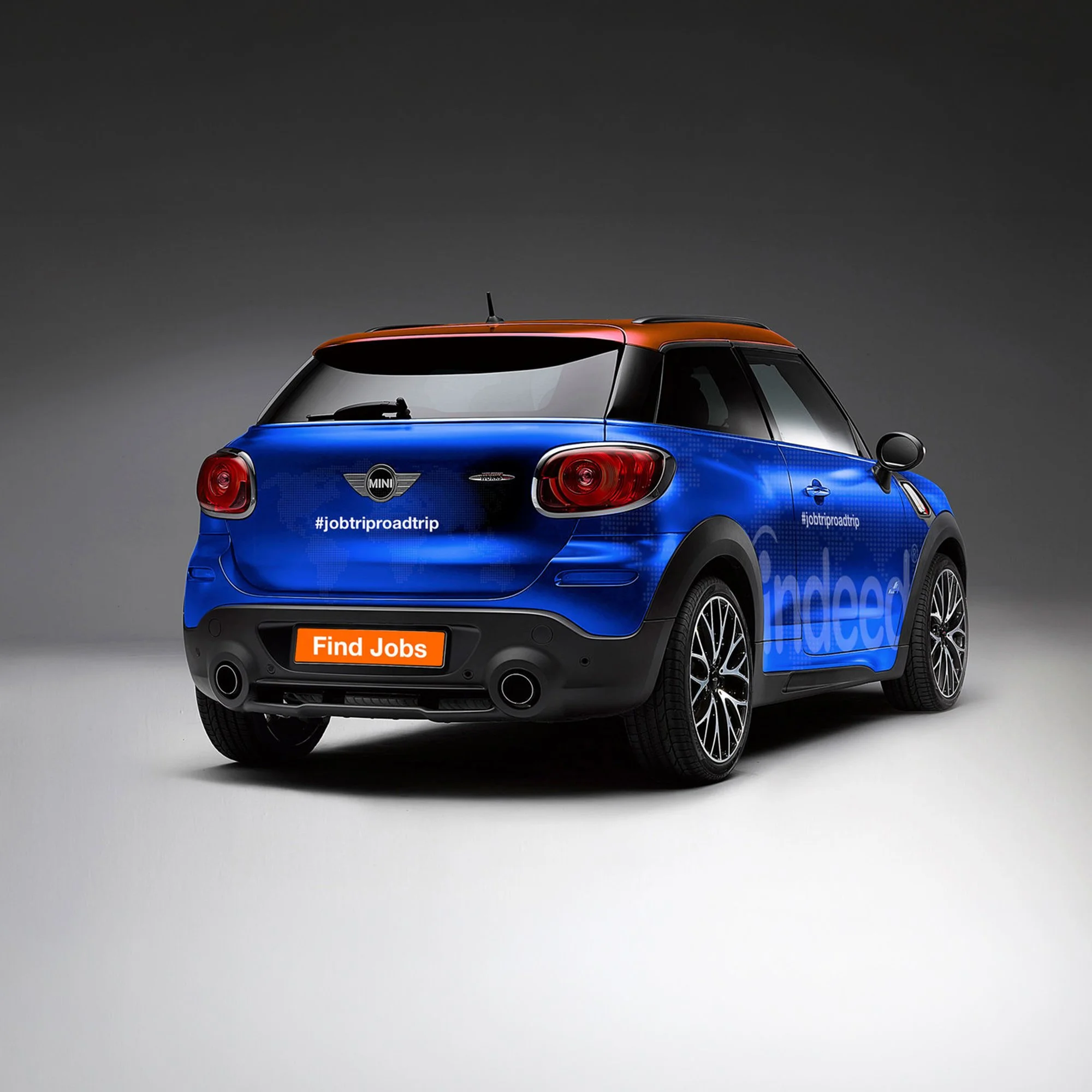 A blue and black compact car with a colorful roof parked on a plain gray background.