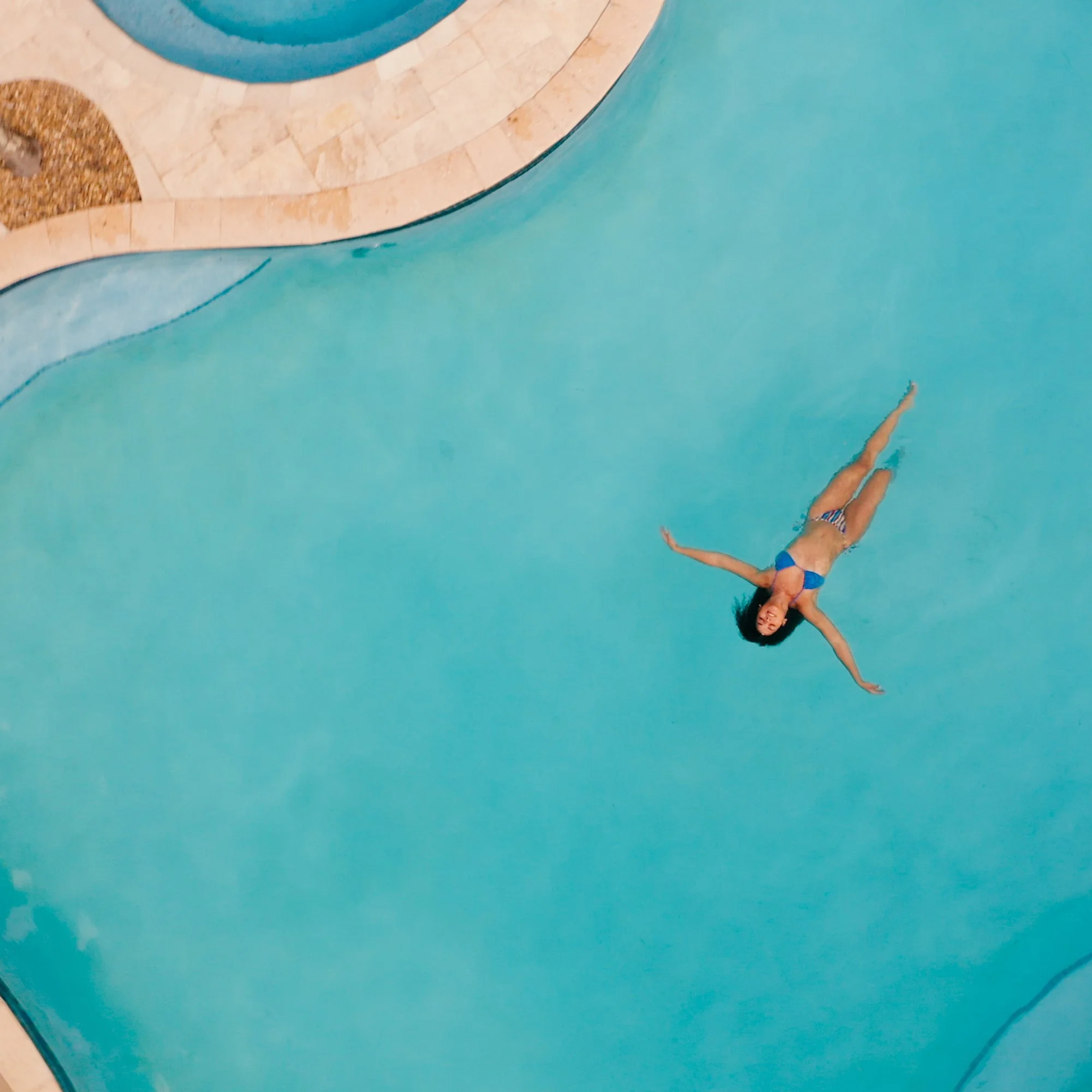 A woman swimming underwater in a bright blue swimming pool, wearing a striped swimsuit.