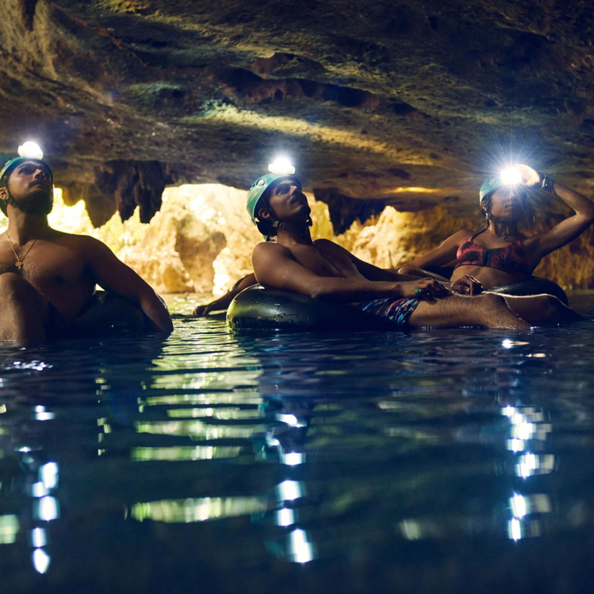 People wearing helmets and headlamps exploring a cave, with a rocky ceiling overhead and water at their feet.