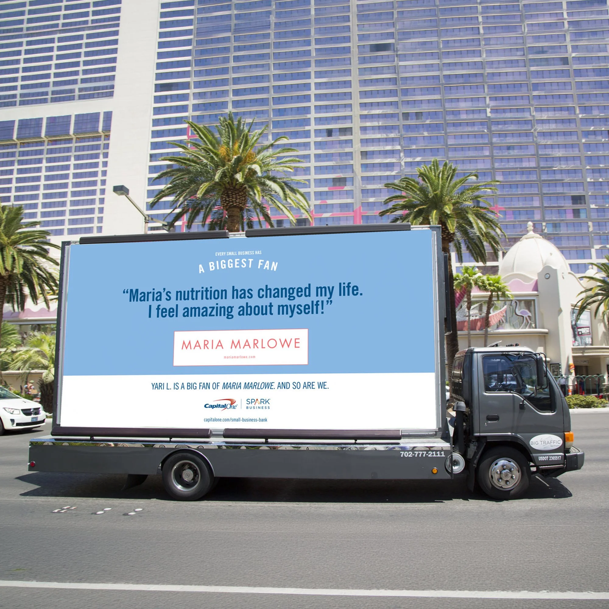 A truck with an advertisement on it reads, 'Maria's nutrition has changed my life. I feel amazing about myself' and features a quote from Yari L., with a background of tall glass buildings and palm trees under a clear blue sky.