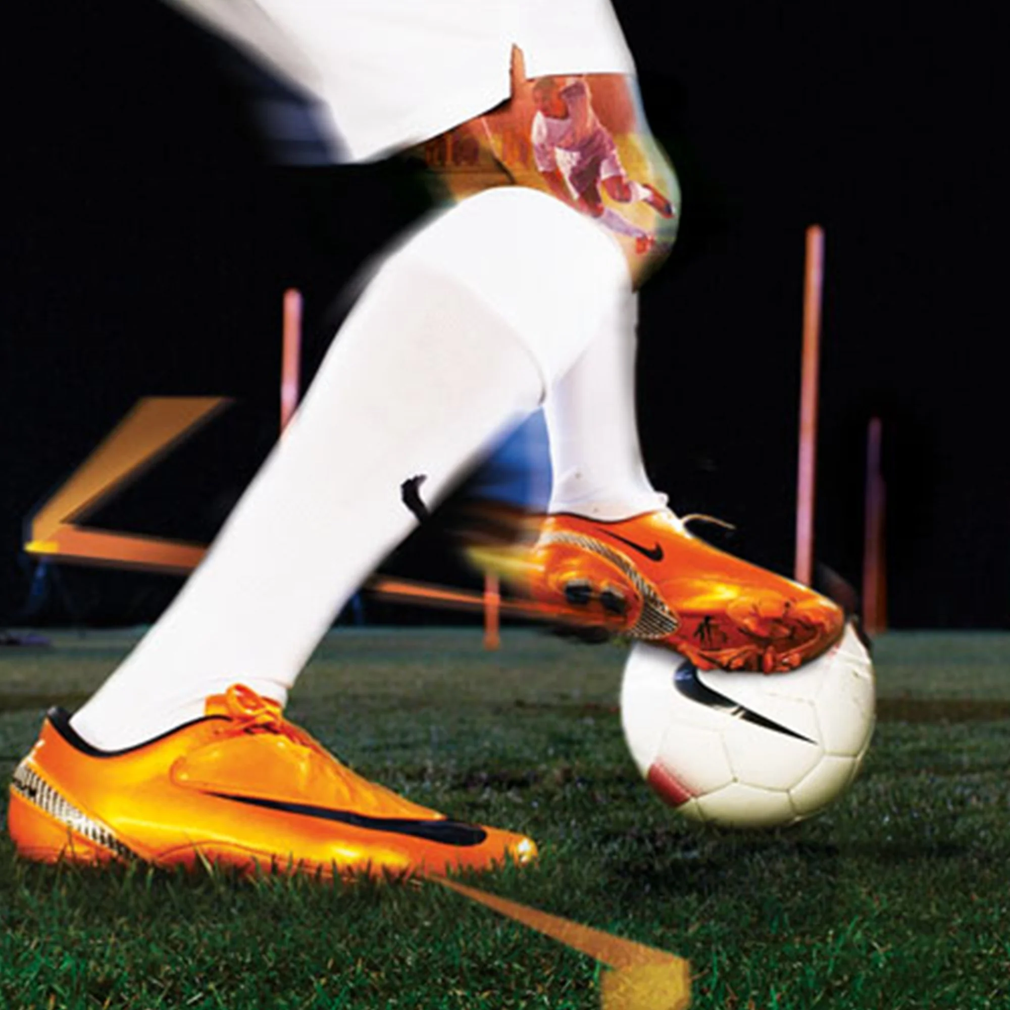 Close-up view of a soccer player's foot in orange cleats making contact with a white soccer ball on a grass field, with focus on the shoes and ball.