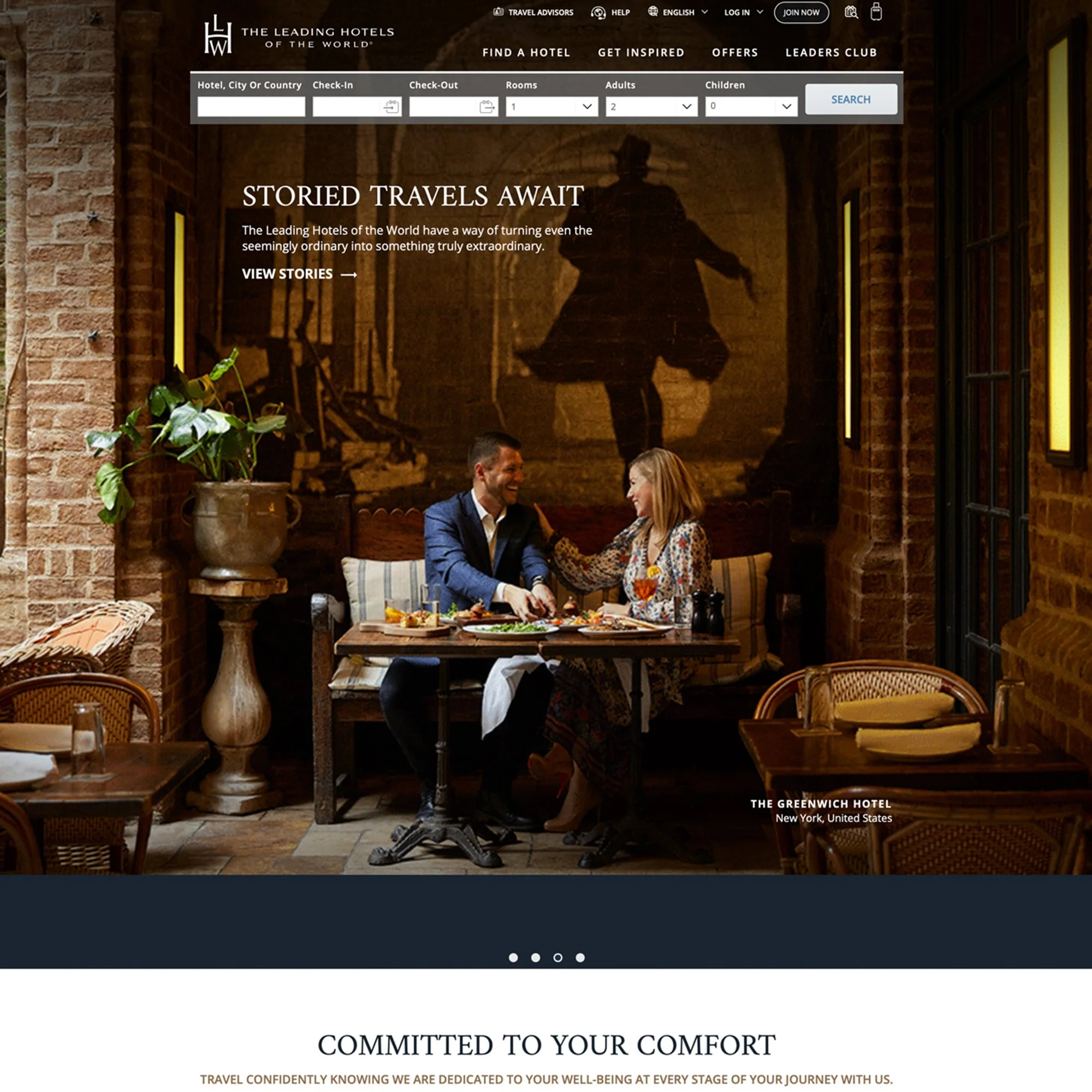 Smiling man and woman sitting at a table with food and drinks in a cozy, brick-walled restaurant or hotel lounge.
