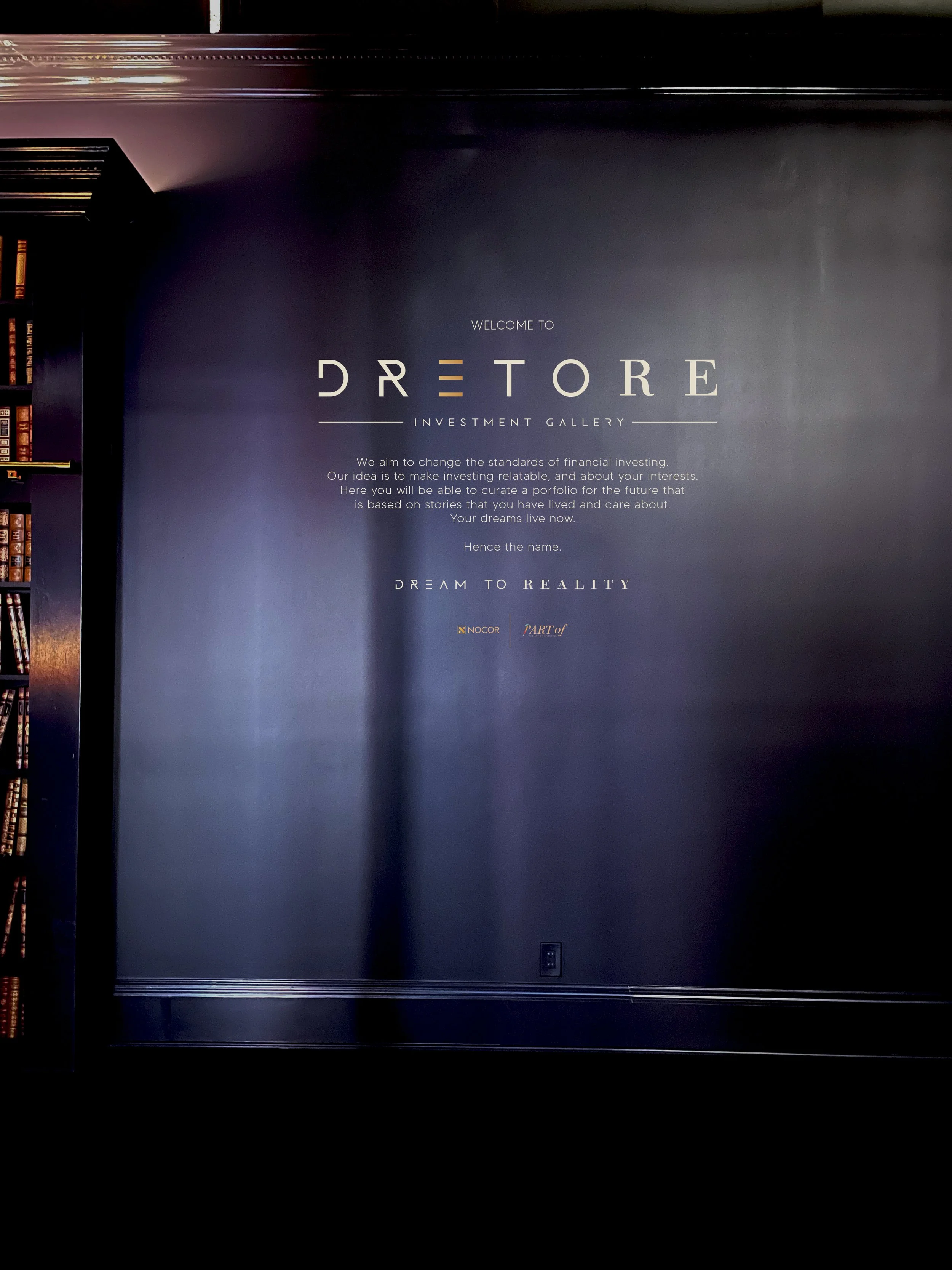 A dark wall with a sign that says "Welcome to DRE Store Investment Gallery" and a paragraph explaining the goal to change financial investing standards and help people build their future based on stories from their lives.