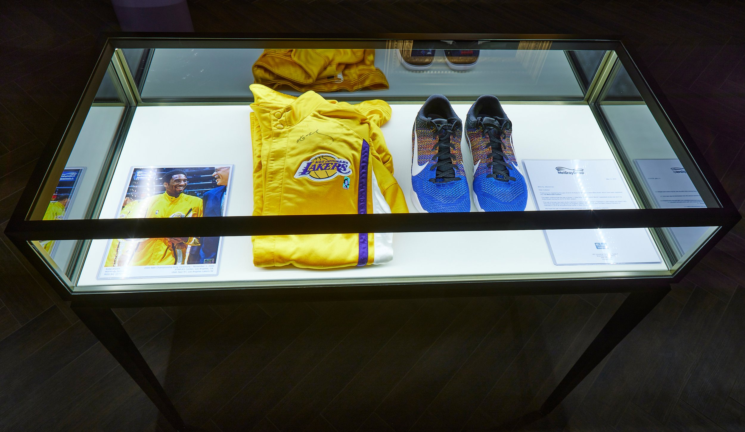 Display case with a yellow Los Angeles Lakers jacket, a pair of colorful Nike sneakers, a signed photograph of a Lakers player, and informational cards.