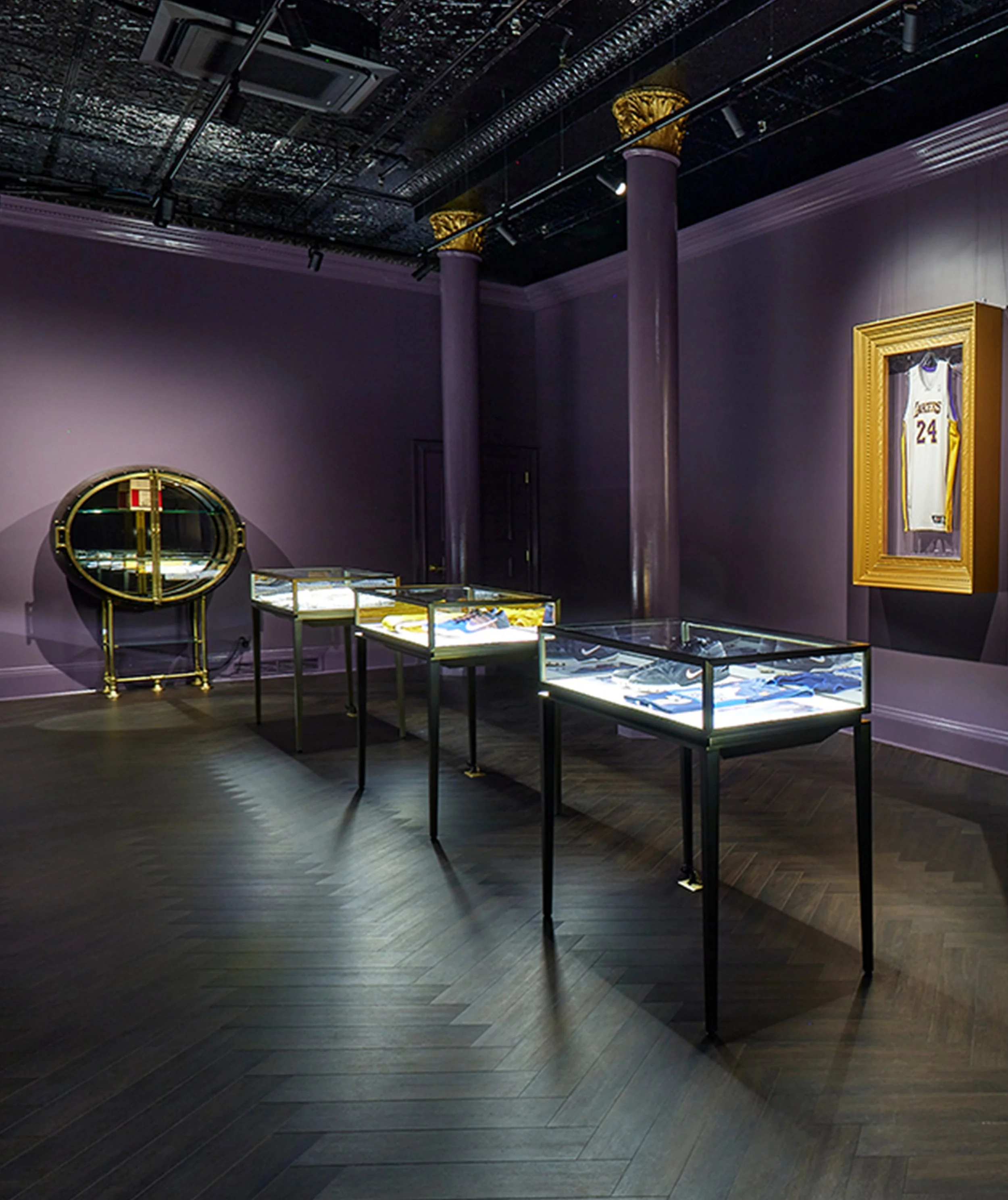 An interior exhibition space with display cases in the center, purple walls, gold accents, and a framed sports jersey on the wall.