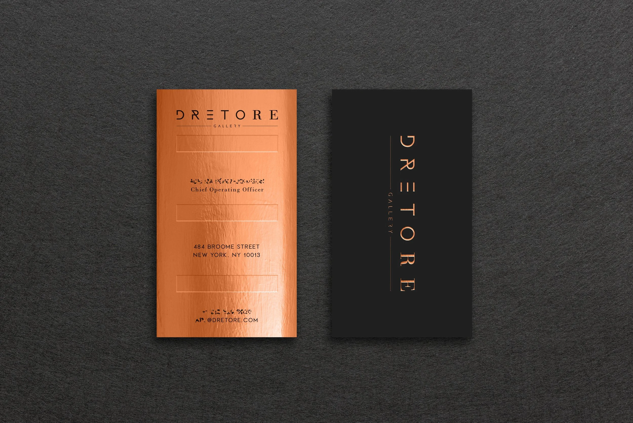 Close-up of two business cards placed side by side on a black surface. The left card is copper-colored with black text, and the right card is black with copper-colored text. The cards display the name 'DRETTORE' and related information.