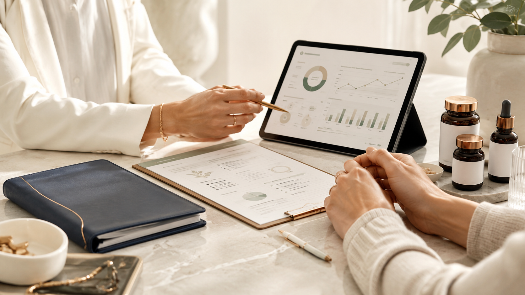 A person using a tablet with financial graphs, surrounded by documents, bottles, and a pen, in a workspace with a potted plant.