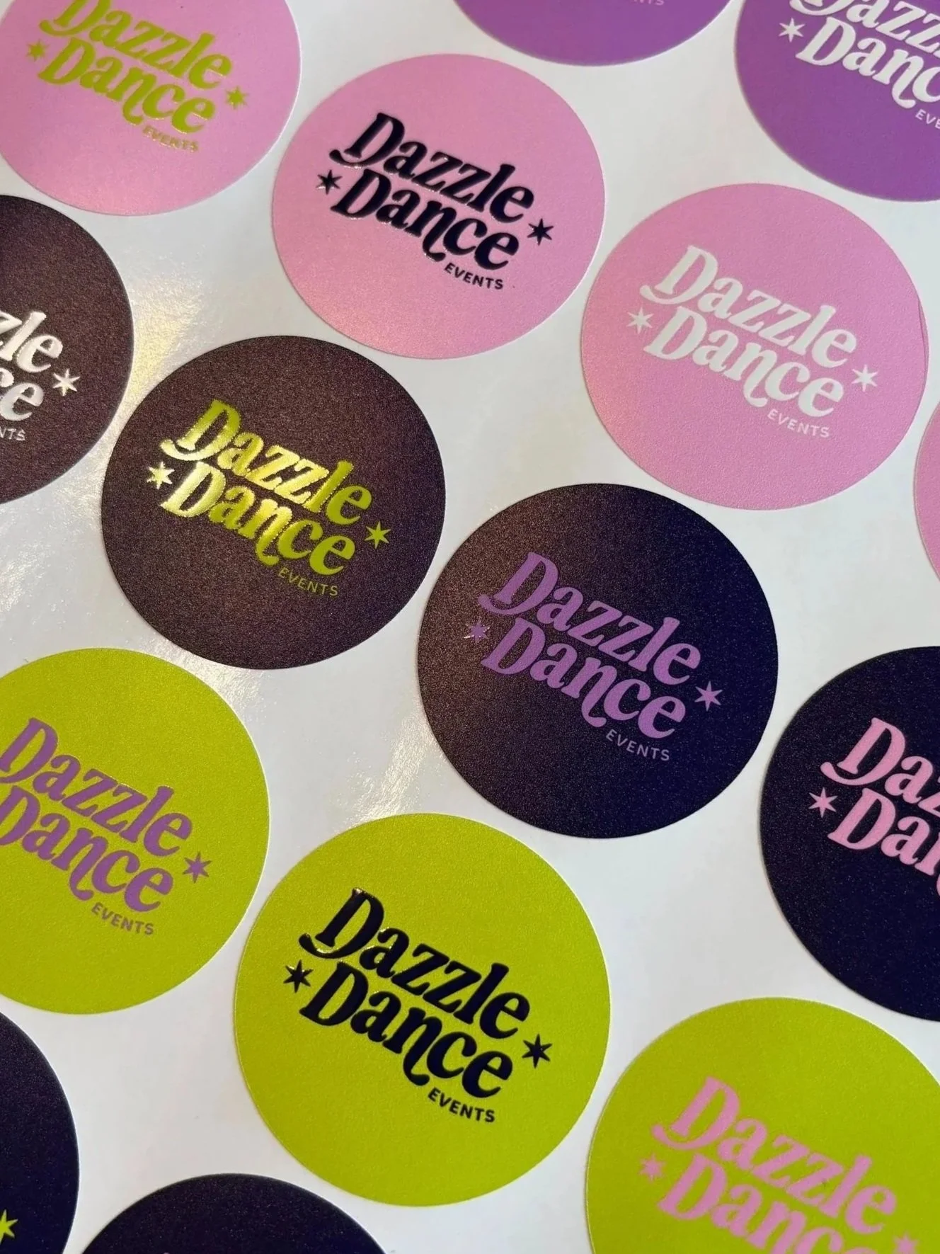 A sheet of colorful stickers featuring the logo 'Dazzle Dance Events' in various fonts and colors including pink, purple, yellow, and black.