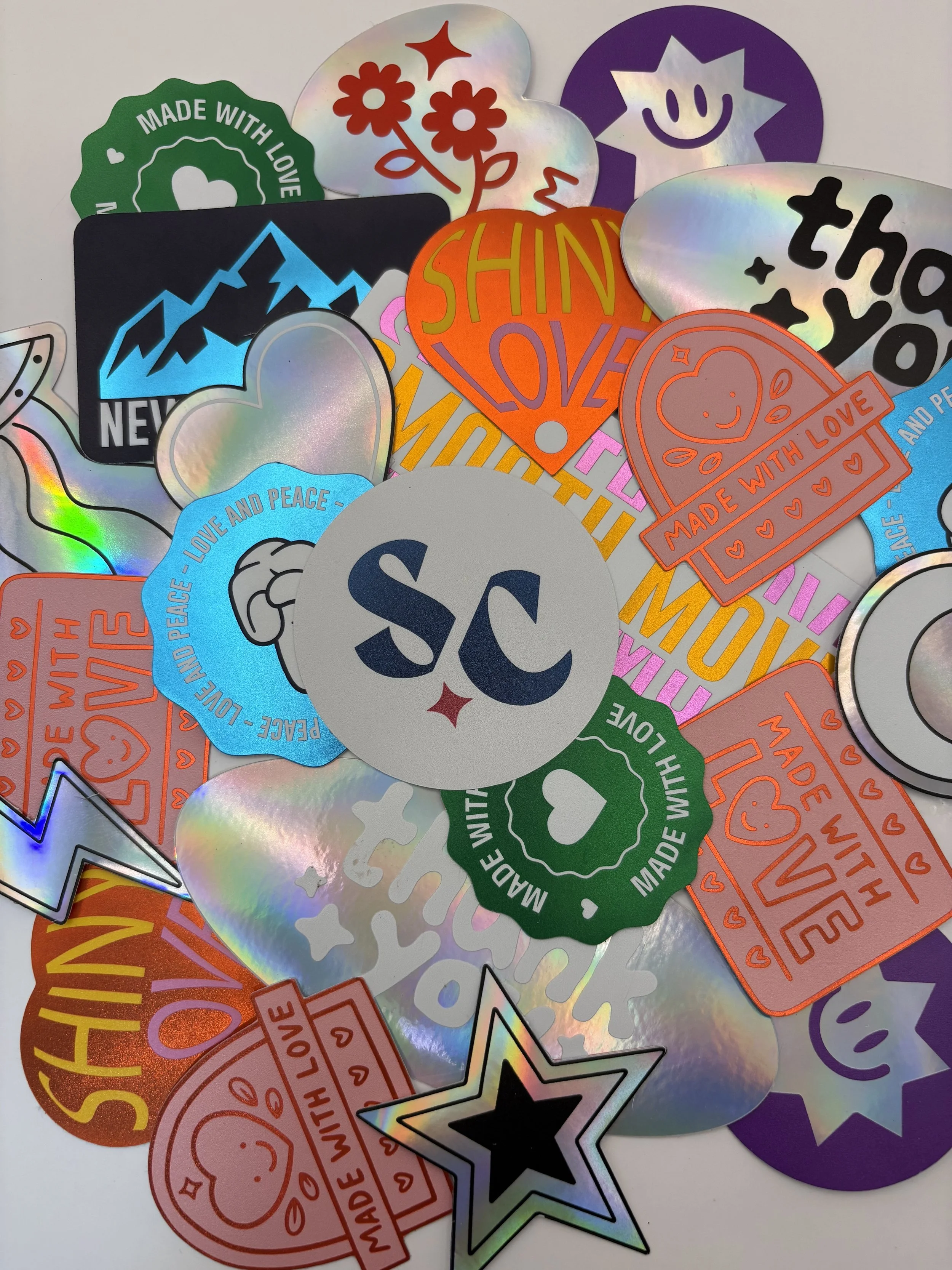 A collection of colorful stickers with various designs, including hearts, stars, mountains, clouds, and text such as 'Shine Love,' 'Made with Love,' 'Peace and Love,' and 'SC.'